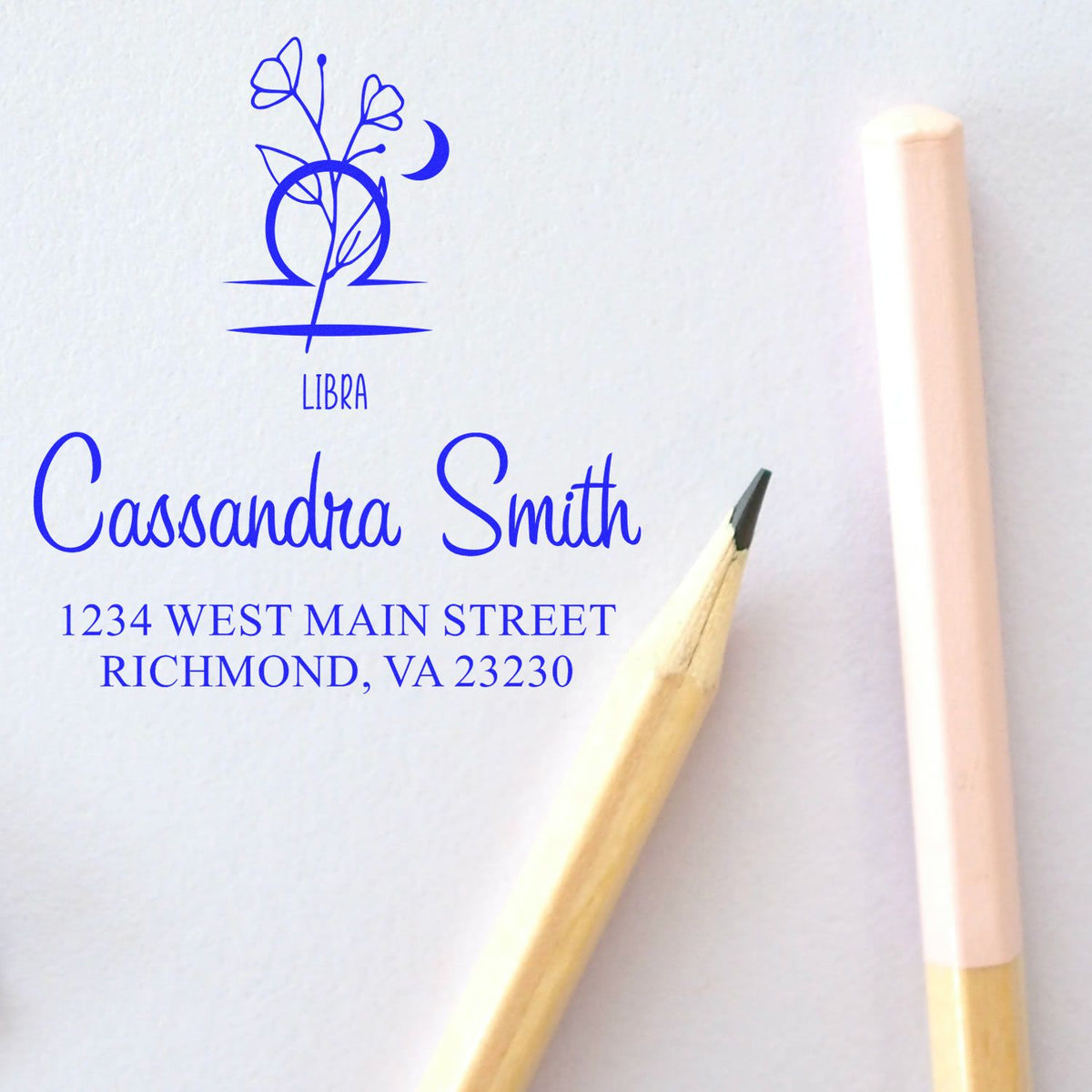 Blue custom Libra stamp seal with floral emblem, Cassandra Smith name and address on white paper, beside pencil and wax seal stick.