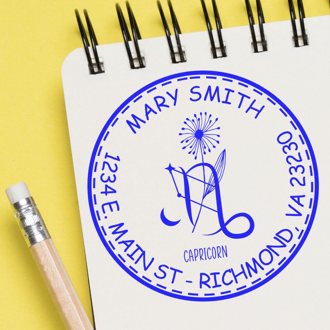Blue custom Capricorn stamp seal for Mary Smith on a white spiral notebook, with yellow background and pencil.