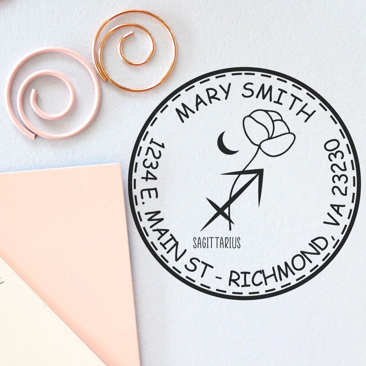 Custom black round address stamp seal with Sagittarius symbol, beside blush pink and gold wax seal rings.