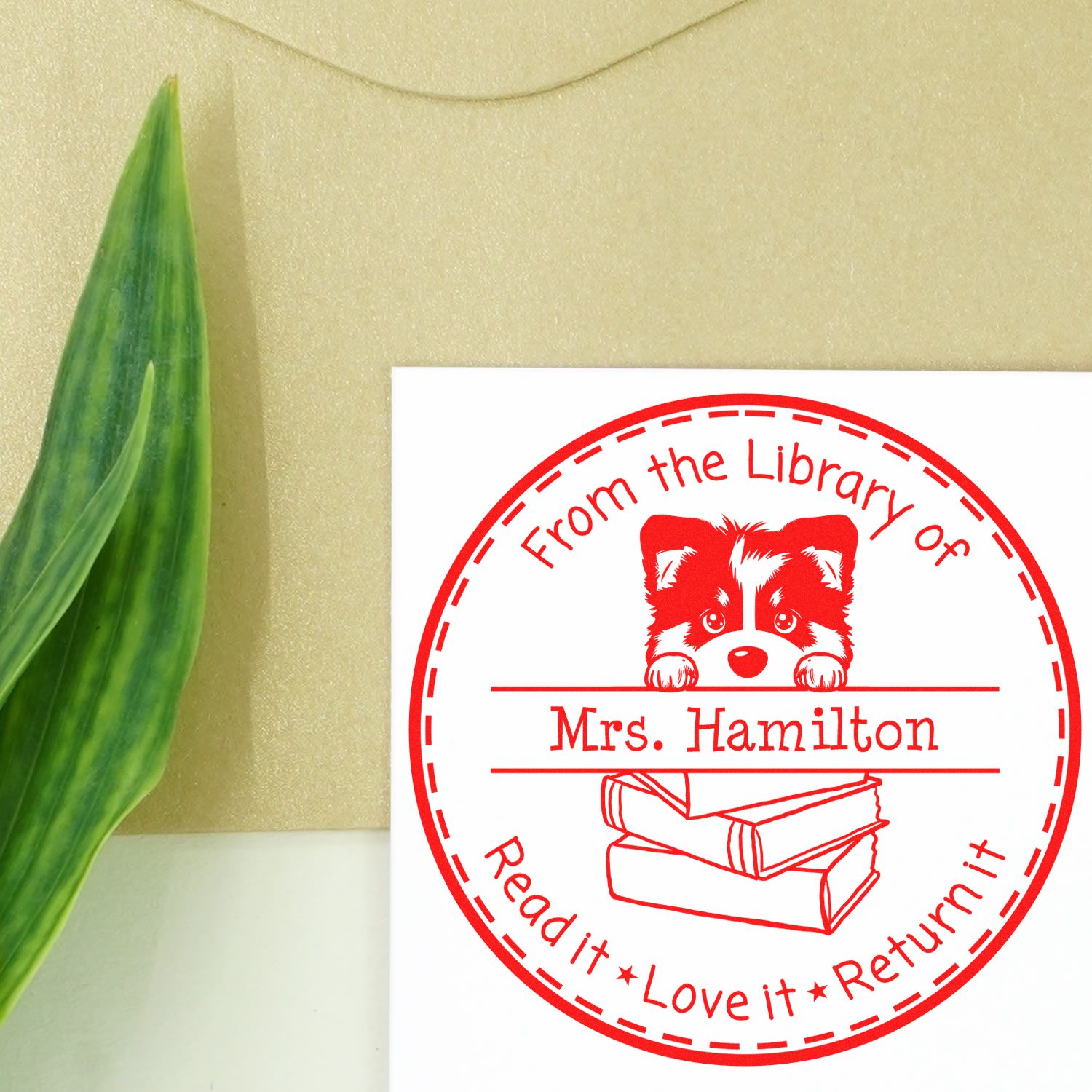 Red circular library return stamp seal with raccoon, books, and Mrs. Hamilton on cream background beside a green leaf