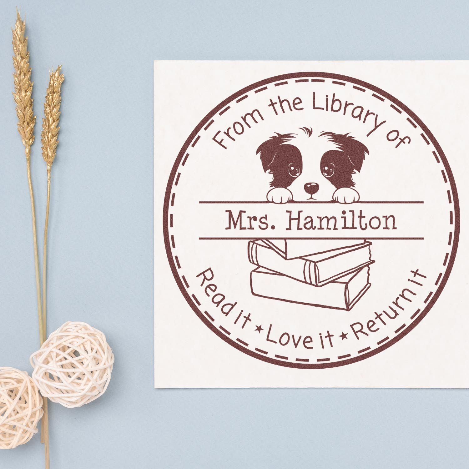 Custom brown rubber stamp seal with puppy and books, Mrs. Hamilton, on a white card against a light blue background.