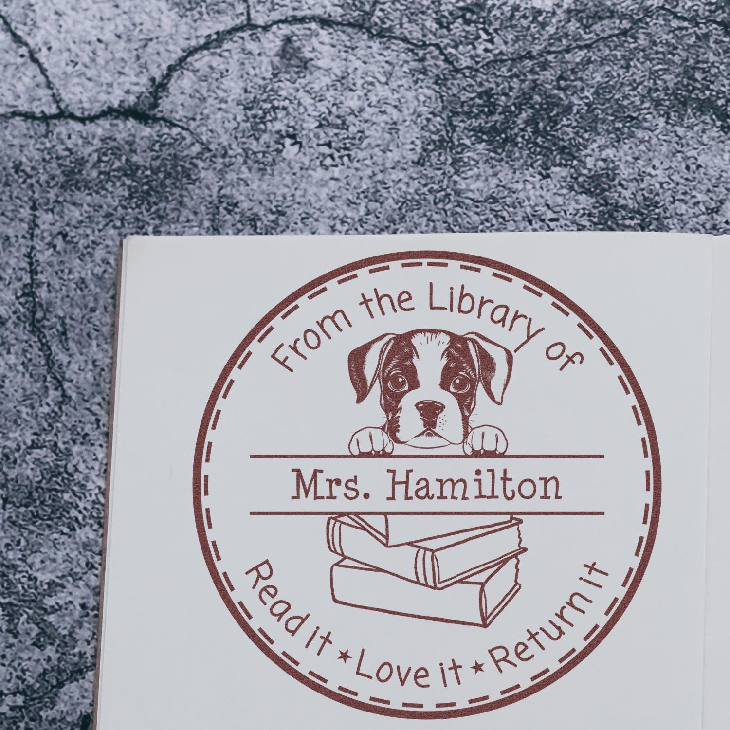 Brown custom library stamp seal with a puppy, stacked books, and Mrs. Hamilton on white paper.