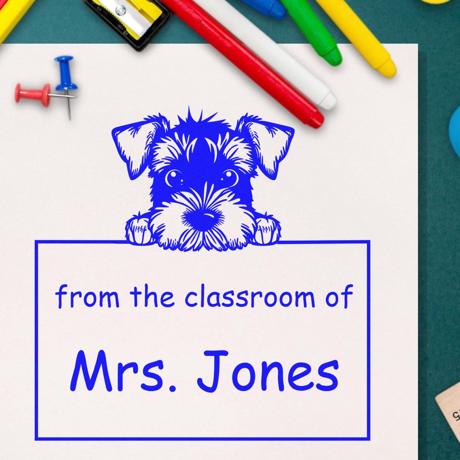 Blue dog classroom stamp and seal reading from the classroom of Mrs. Jones on white paper, with colorful pens and push pins.