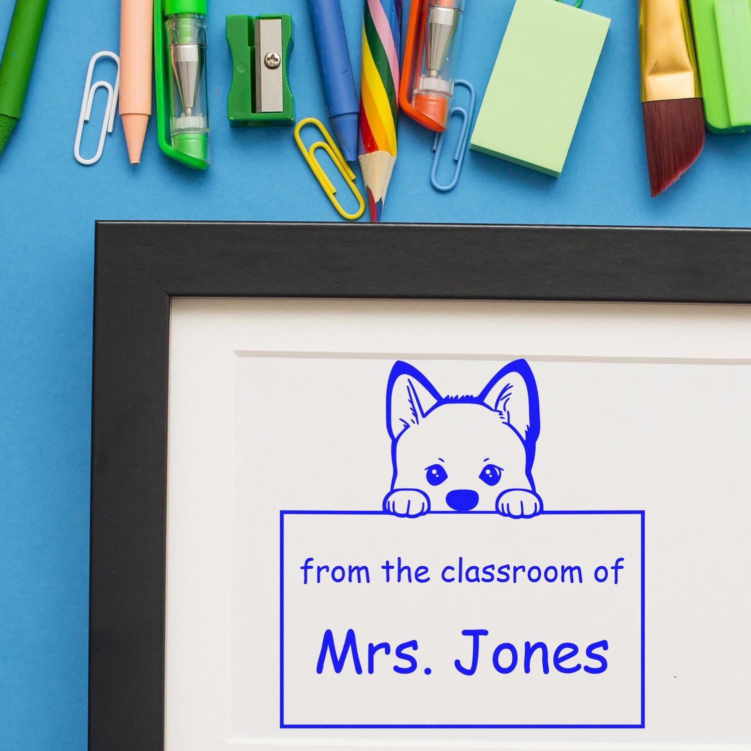 Custom classroom stamp and seal with blue dog design, Mrs. Jones text, on a blue desk with colorful stationery.