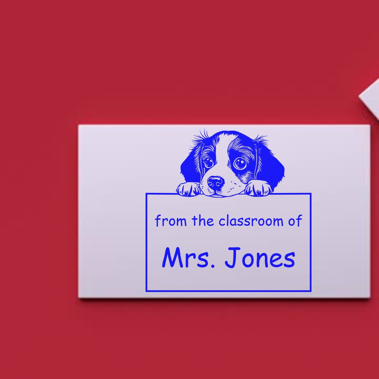 Blue classroom stamp and seal featuring a puppy and from the classroom of Mrs. Jones on a white block against a red background.