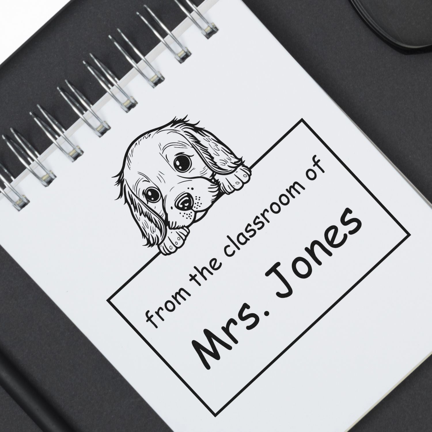 Black-and-white custom stamp and seal with puppy illustration and text, from the classroom of Mrs. Jones, on a spiral notebook.