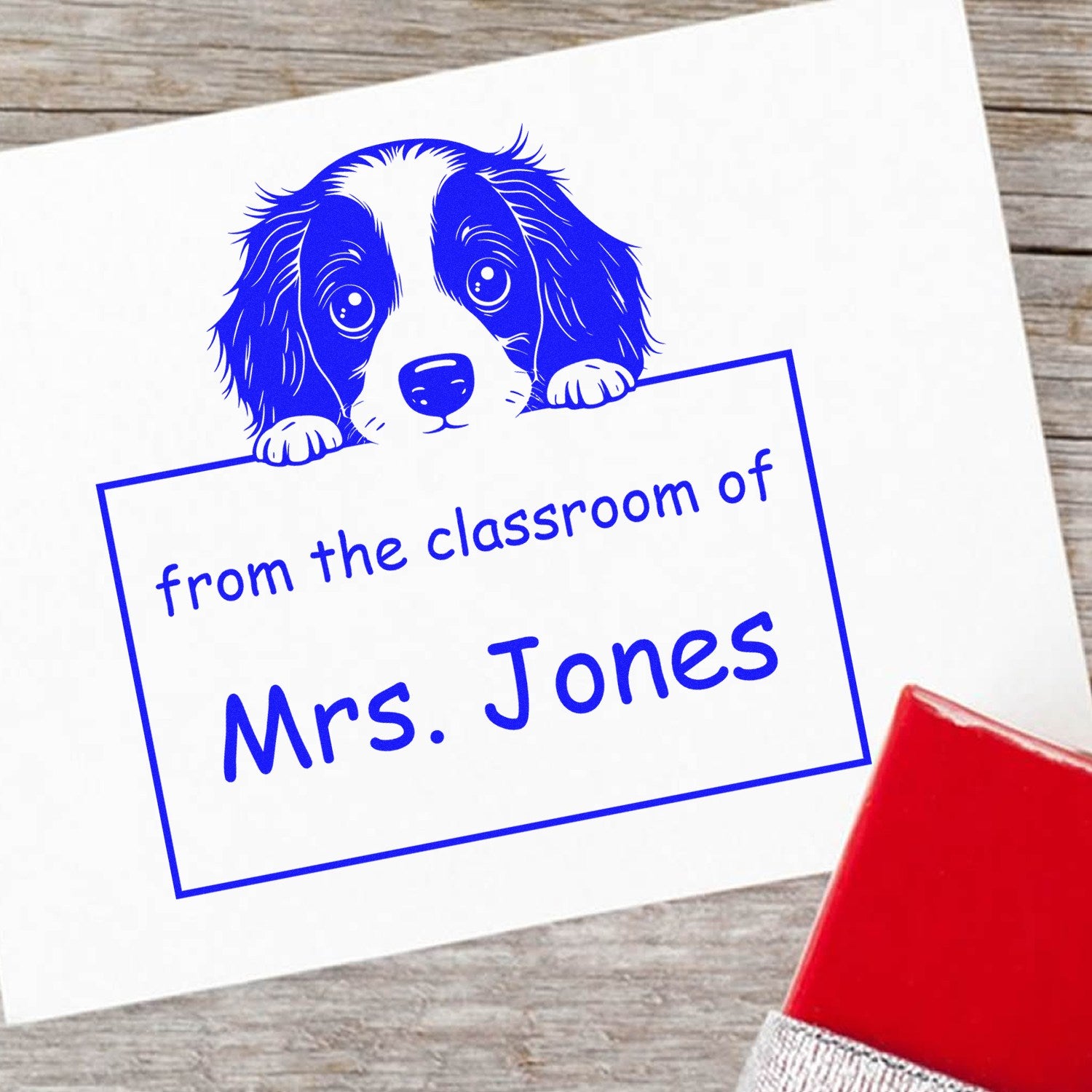 Blue dog classroom stamp and seal with from the classroom of Mrs. Jones in blue on white paper, red stamp handle visible.