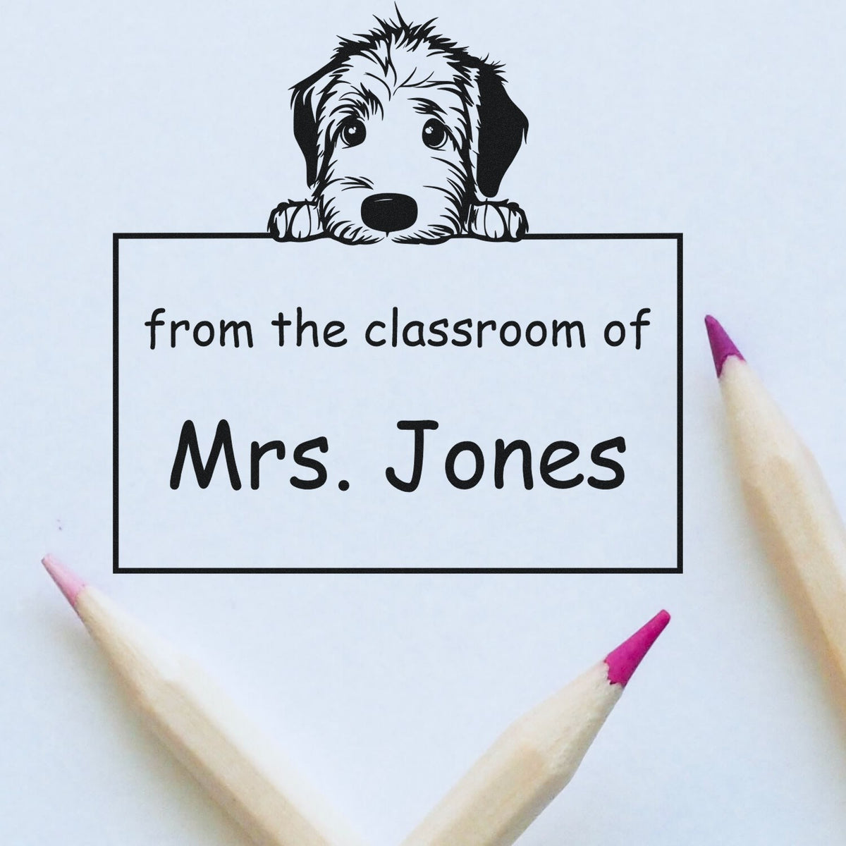 Black dog peeking over custom classroom stamp seal reading from the classroom of Mrs. Jones on white paper with pink pencil tips.