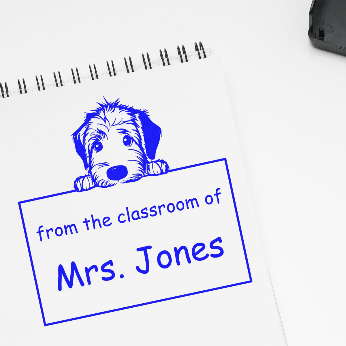 Blue custom stamp seal with dog design and from the classroom of Mrs. Jones on a white spiral notebook.