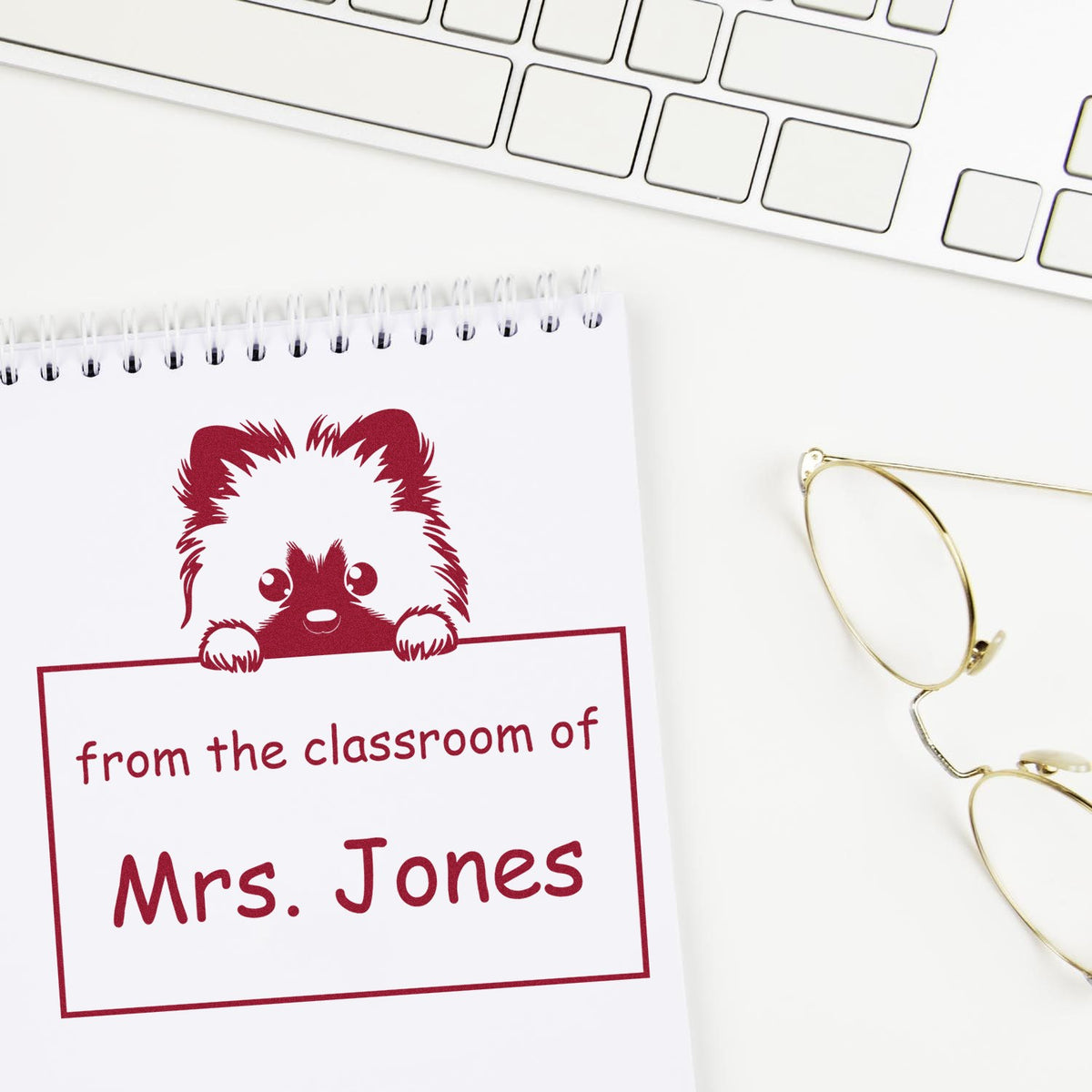 Red classroom stamp seal with cartoon dog and from the classroom of Mrs. Jones on white notebook, beside gold glasses.