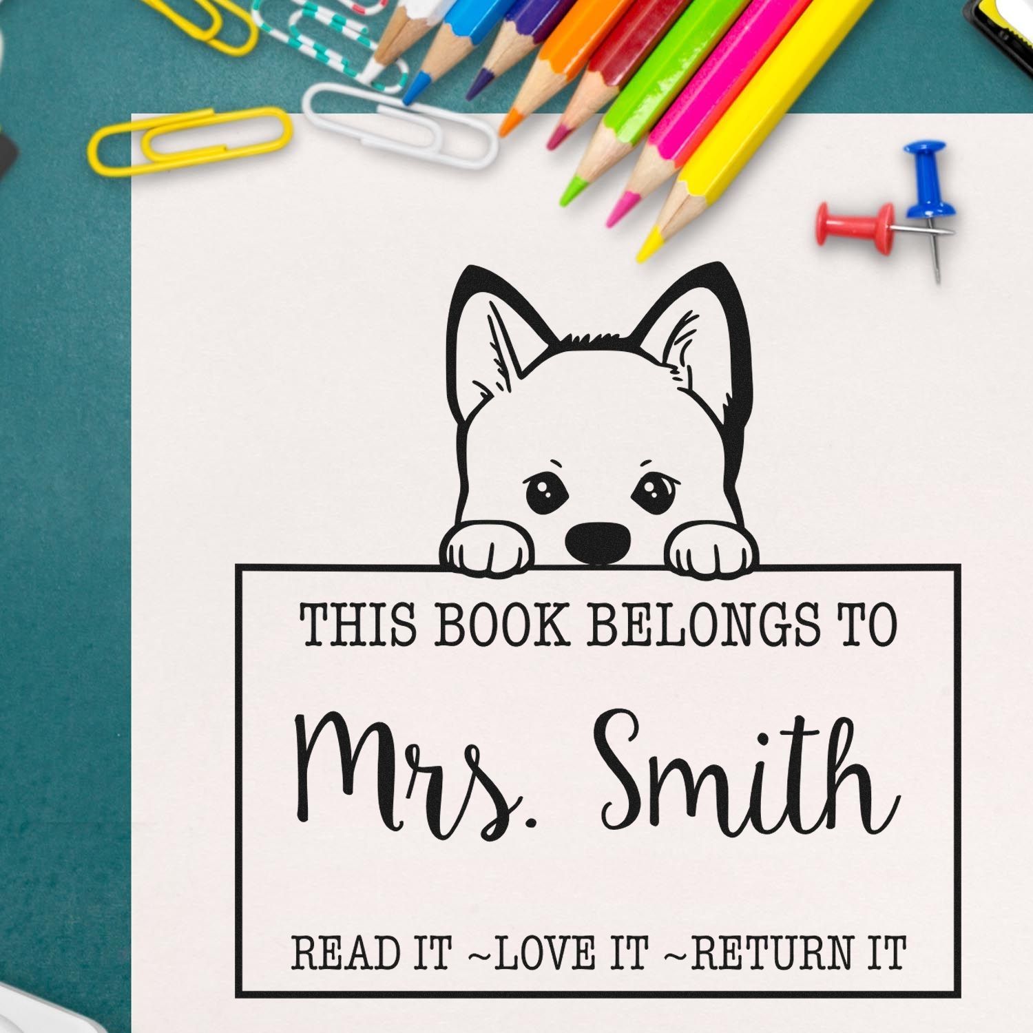 Dog bookplate stamp and seal with black text for This Book Belongs to Mrs. Smith, surrounded by colorful pencils, clips and pins.