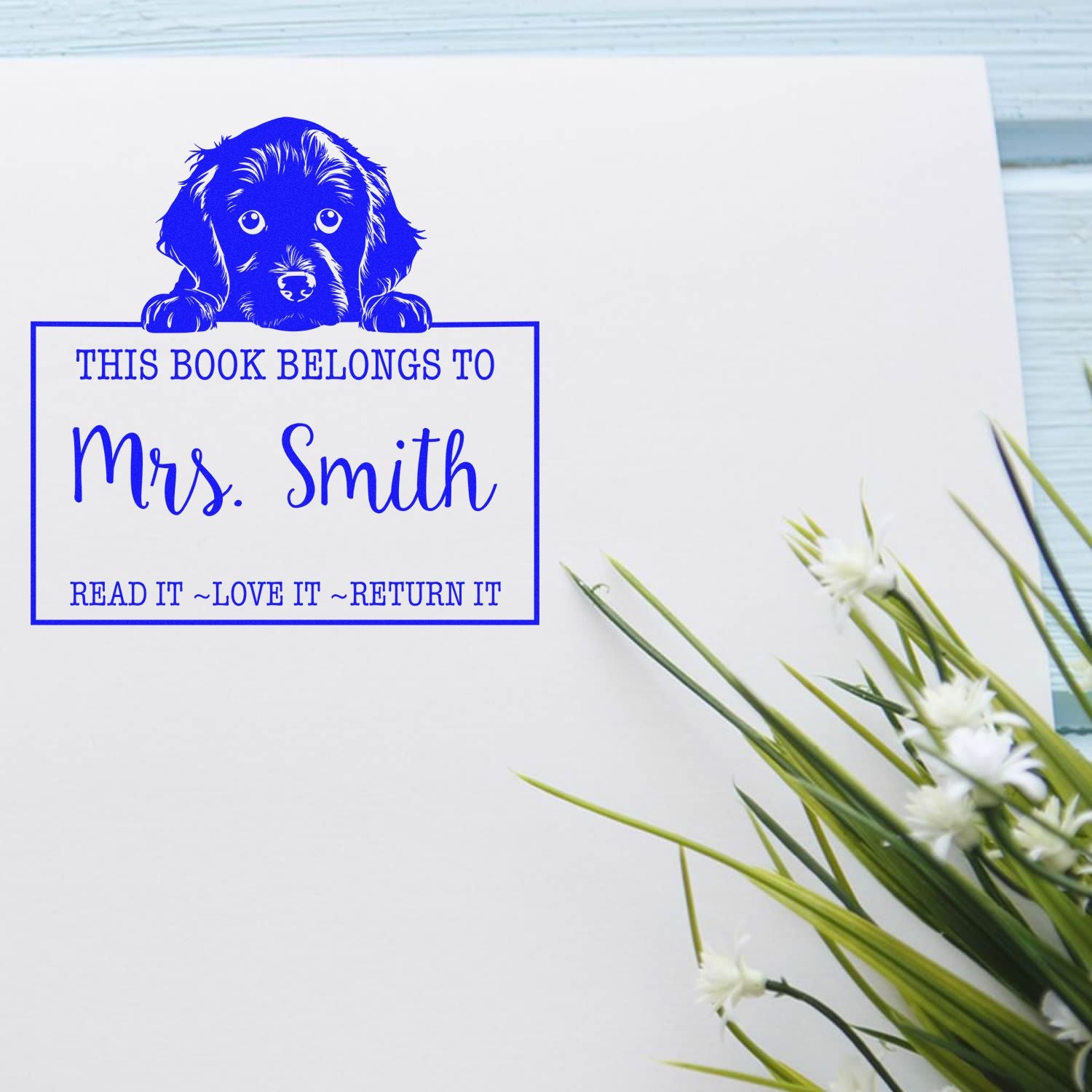 Blue custom book stamp and seal with dog graphic and This Book Belongs to Mrs. Smith on white paper.