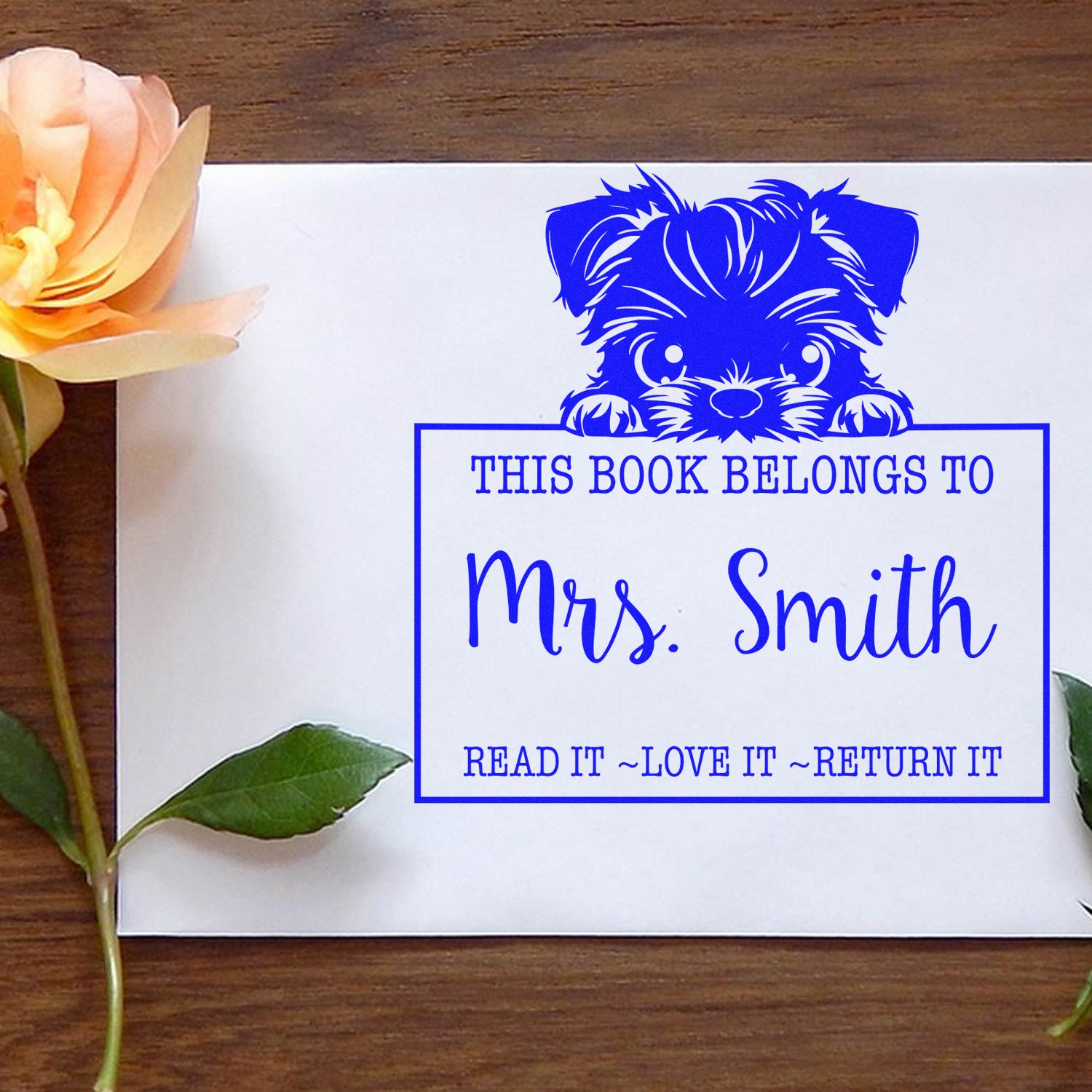 Blue personalized bookplate stamp seal with puppy, reading This book belongs to Mrs. Smith, on white card with peach flower.