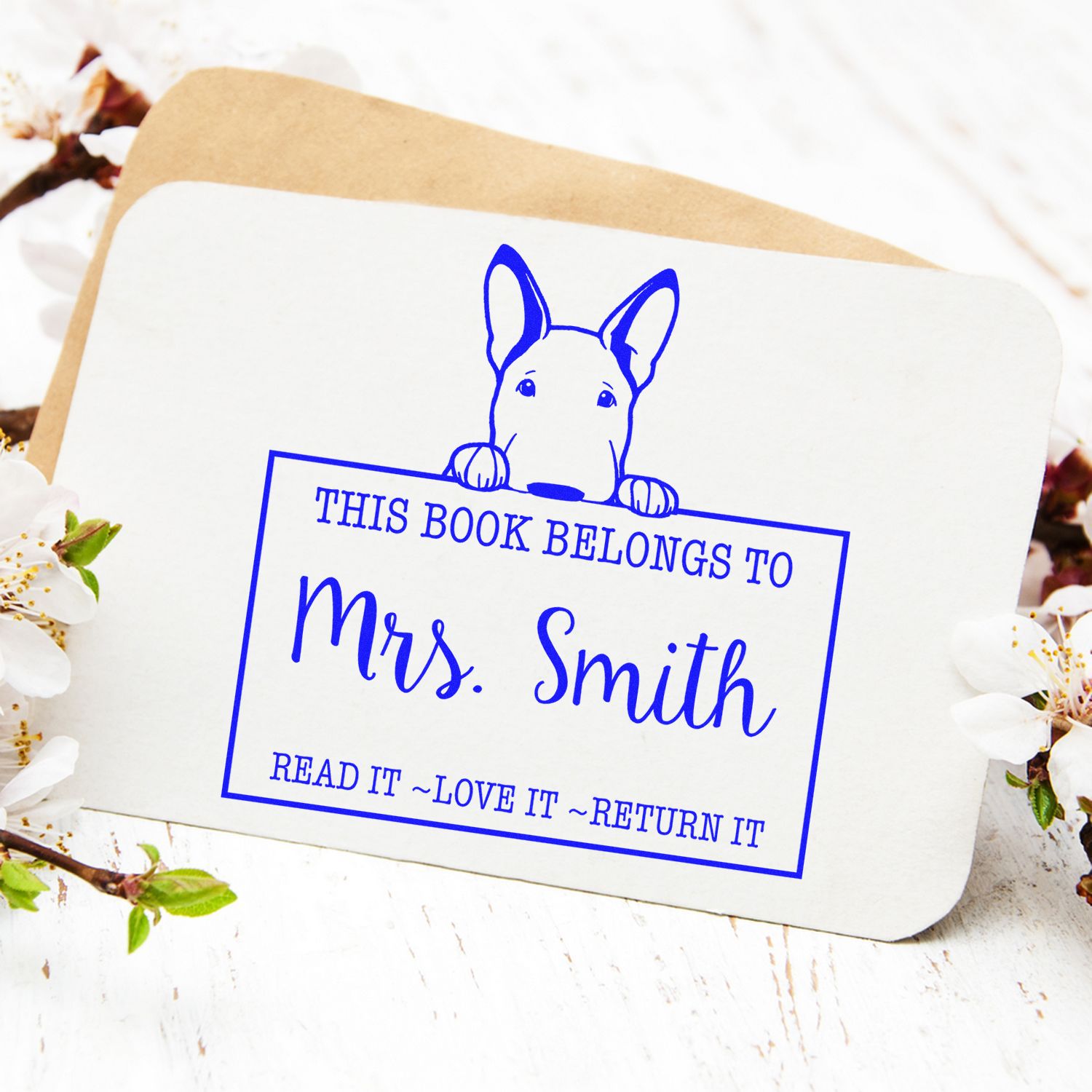 Blue book stamp seal with dog illustration and This Book Belongs to Mrs. Smith on white card