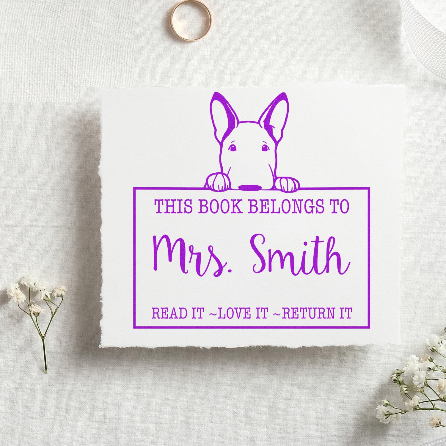 Purple custom book stamp seal with dog illustration and This Book Belongs to Mrs. Smith on white paper.