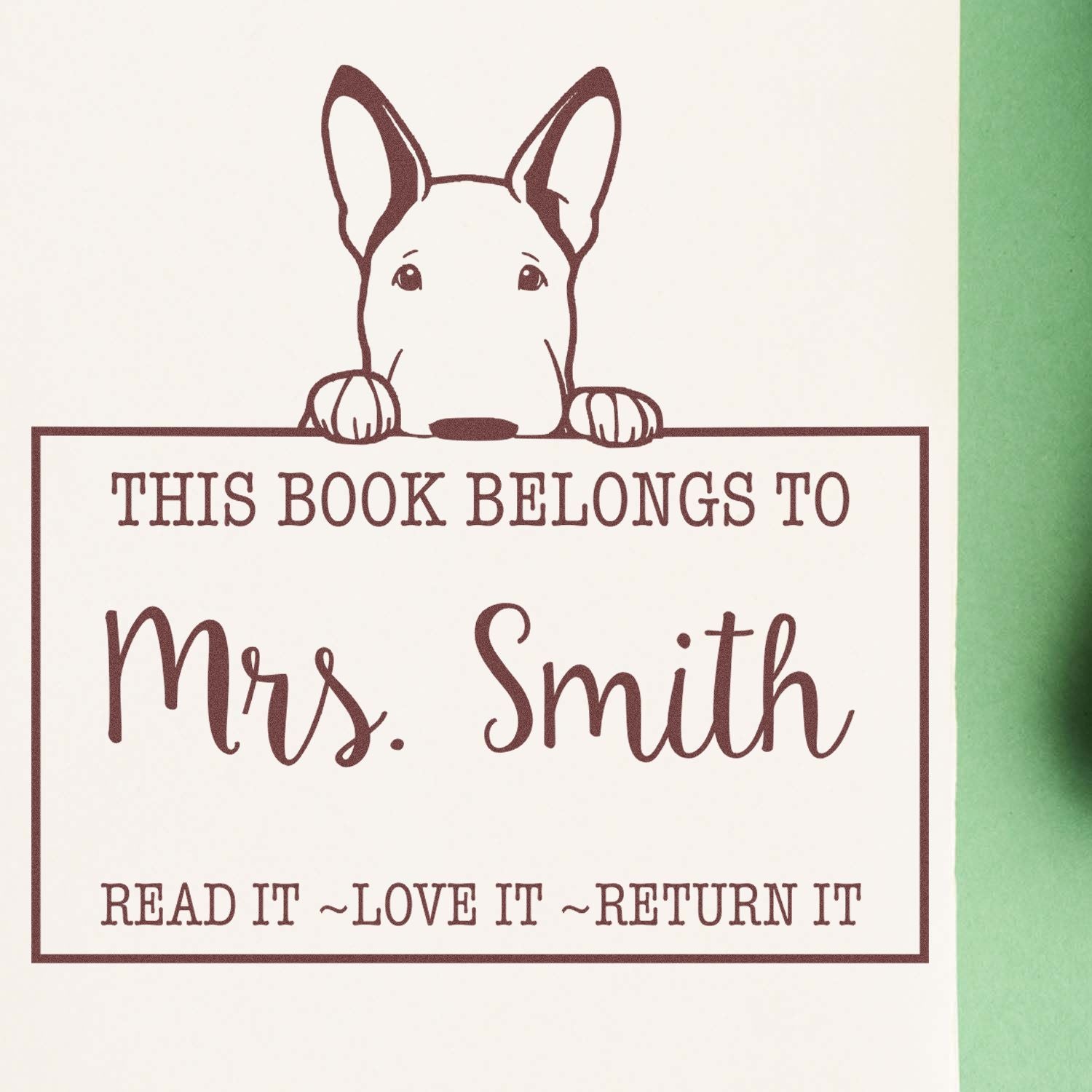 Brown dog bookplate stamp with a dog peeking over This Book Belongs to Mrs. Smith on cream paper, brown ink, green edge.