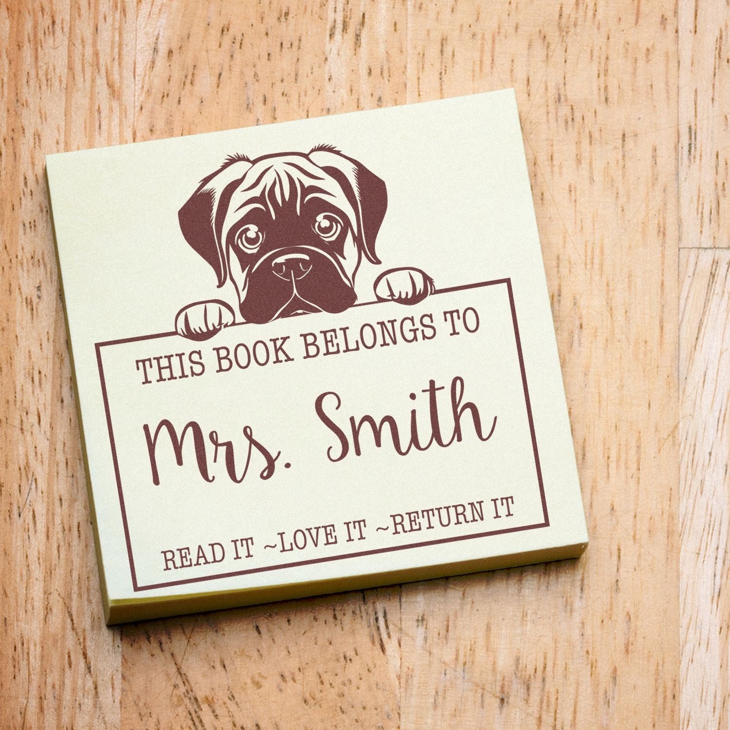 Brown puppy bookplate stamp seal on cream square, reading This Book Belongs to Mrs. Smith in burgundy text on wood background.