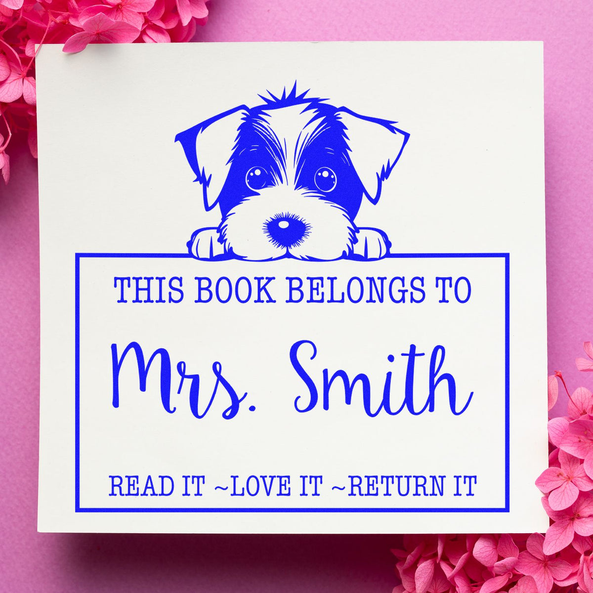 Blue custom book stamp with a dog design, This Book Belongs to Mrs. Smith, in blue on white, framed by pink flowers.
