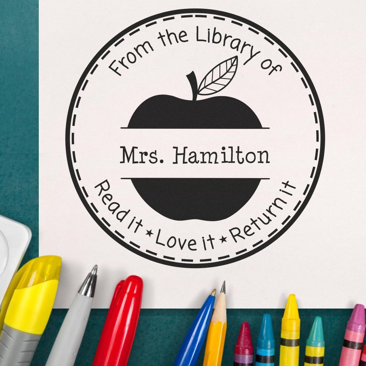 Black circular library stamp seal with apple icon, Mrs. Hamilton, and Read it, Love it, Return it on white paper.