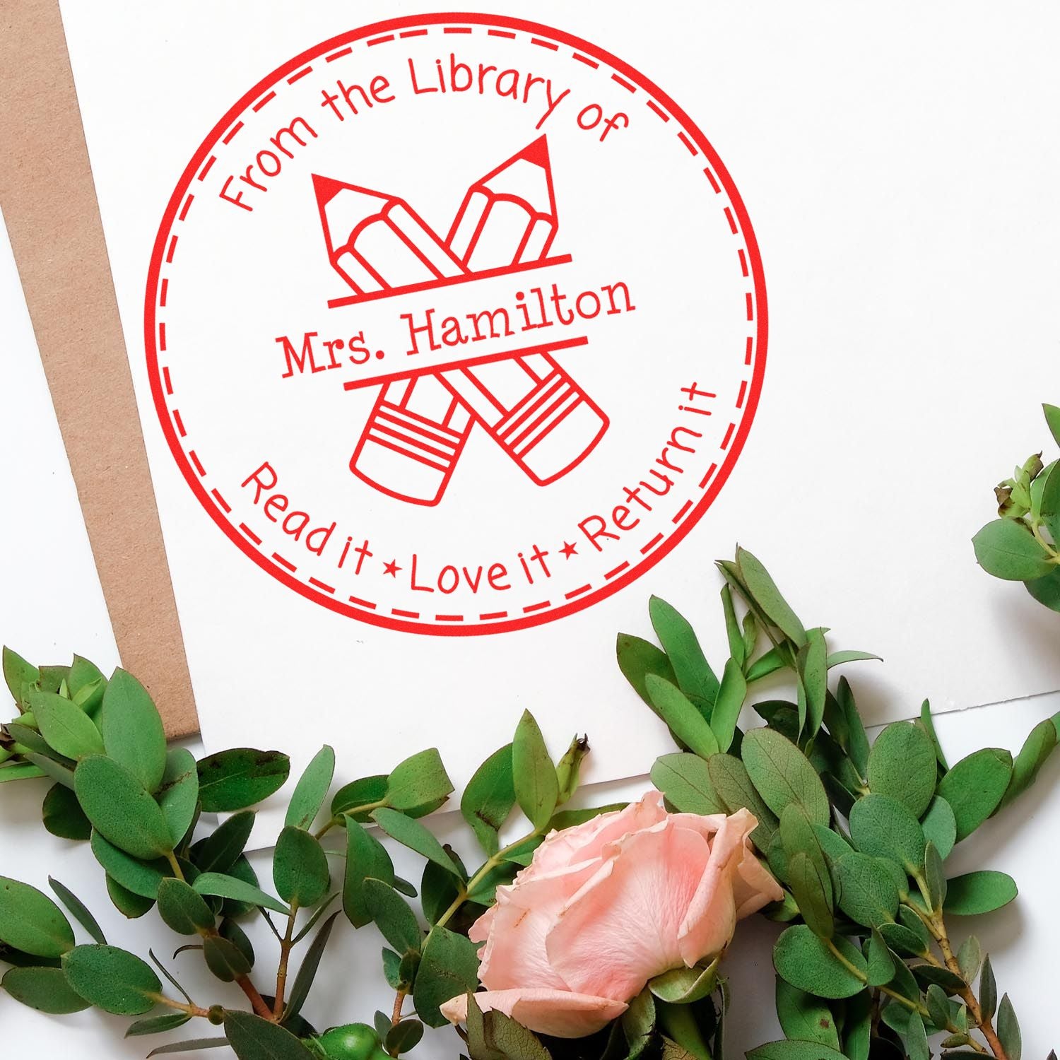 Red circular library return stamp and seal reading From the Library of Mrs. Hamilton with pencils on a white background.