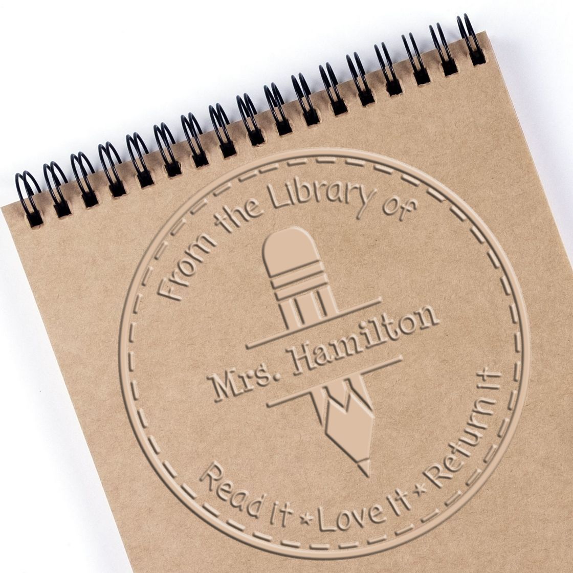 Tan spiral notebook with embossed custom stamp and seal, round library seal, pencil icon, and Mrs. Hamilton in beige.