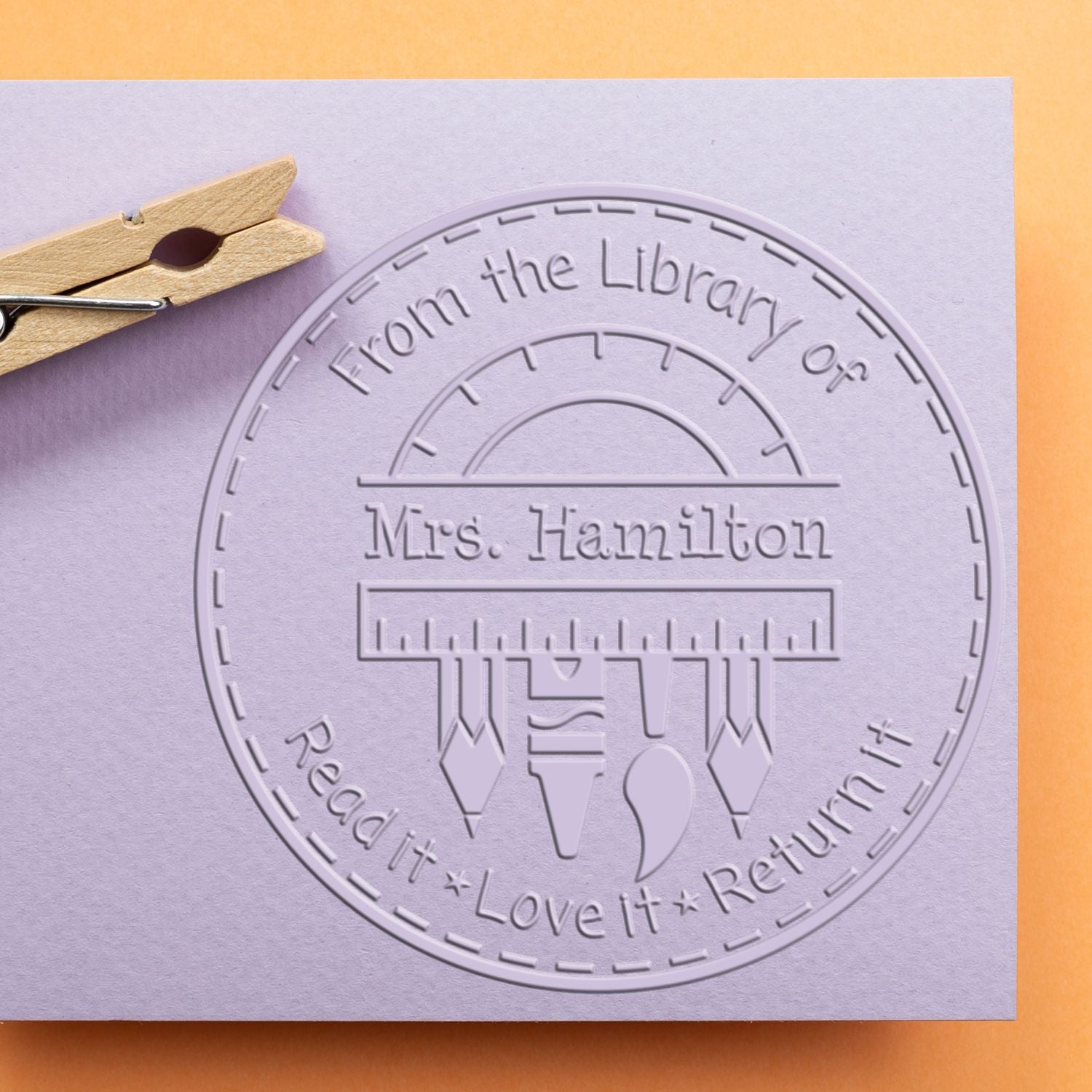 Lavender embossed library return stamp and seal reading From the Library of Mrs. Hamilton, with pencil icons on purple paper.