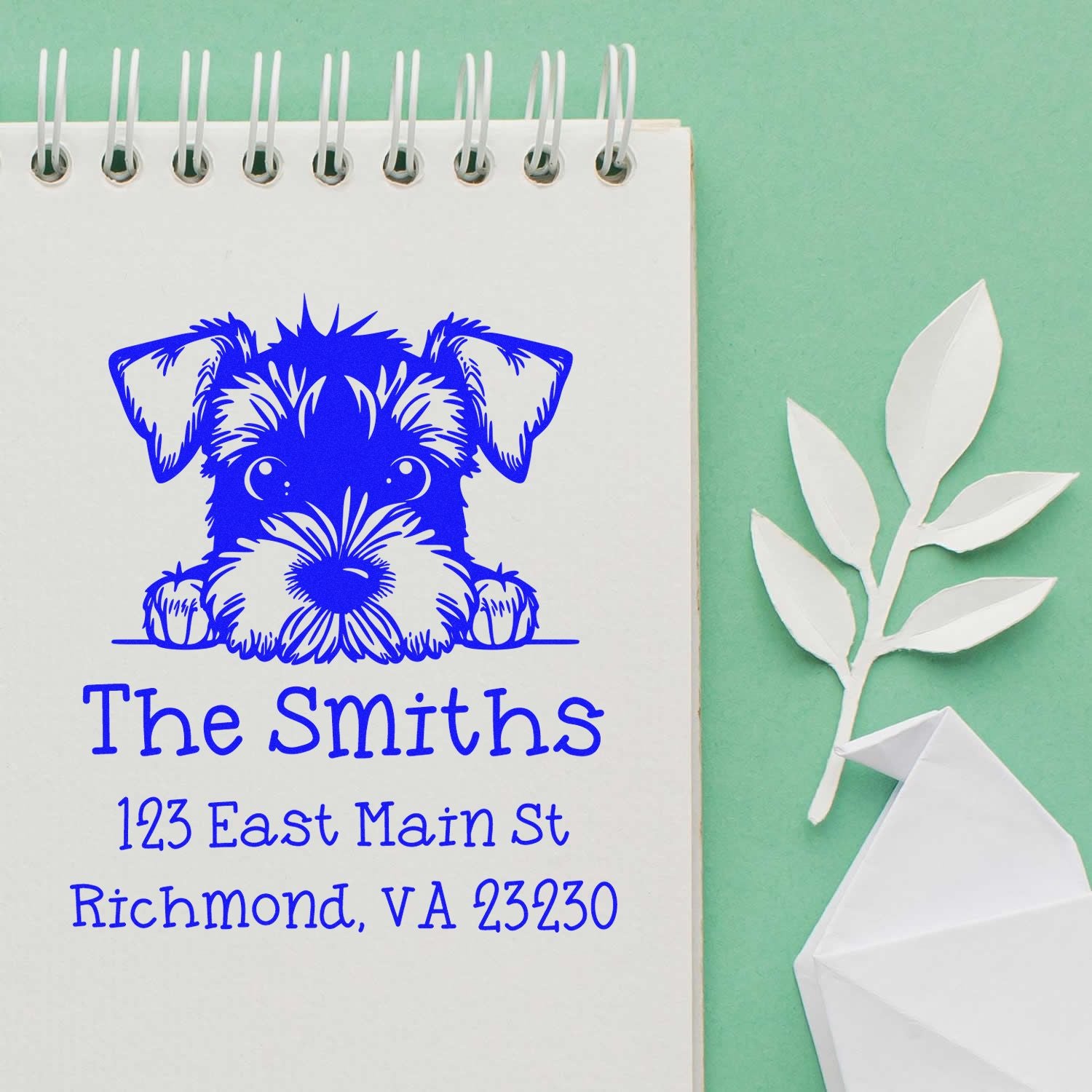 Blue custom address stamp with puppy seal design and The Smiths on a white spiral notebook, on mint green background.
