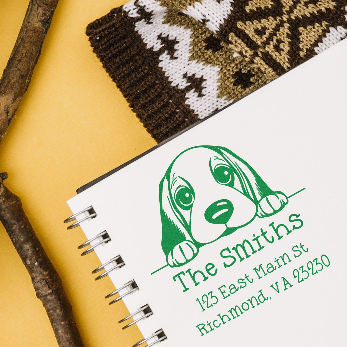 Green custom dog logo stamp on a white spiral notebook, with address text on a yellow background and brown wood accents.