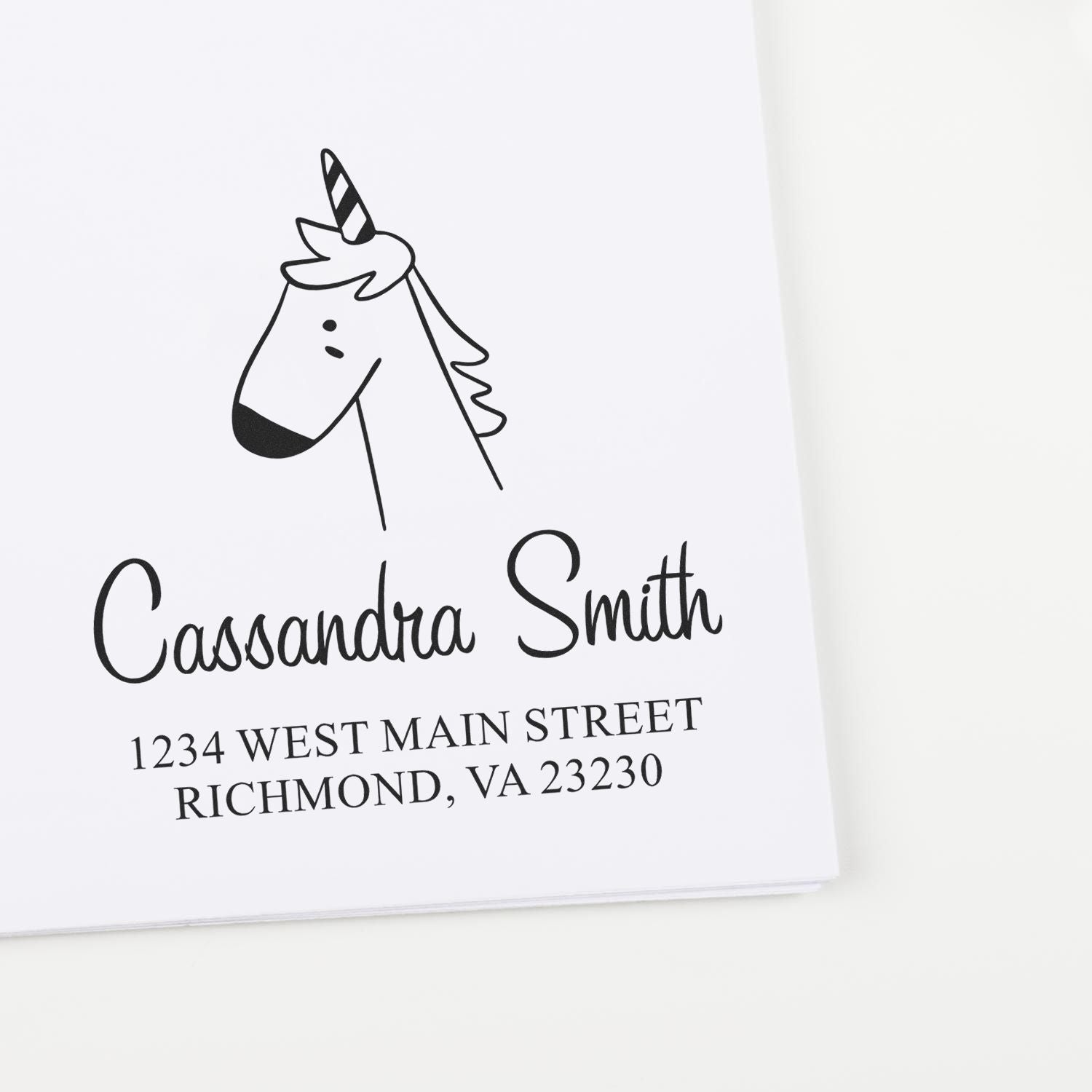 Wood handle whimsical unicorn cartoon animal made to order address stamp on paper. Personalizable address stamp with unicorn illustration and text: "Cassandra Smith, 1234 West Main Street, Richmond, VA 23230."