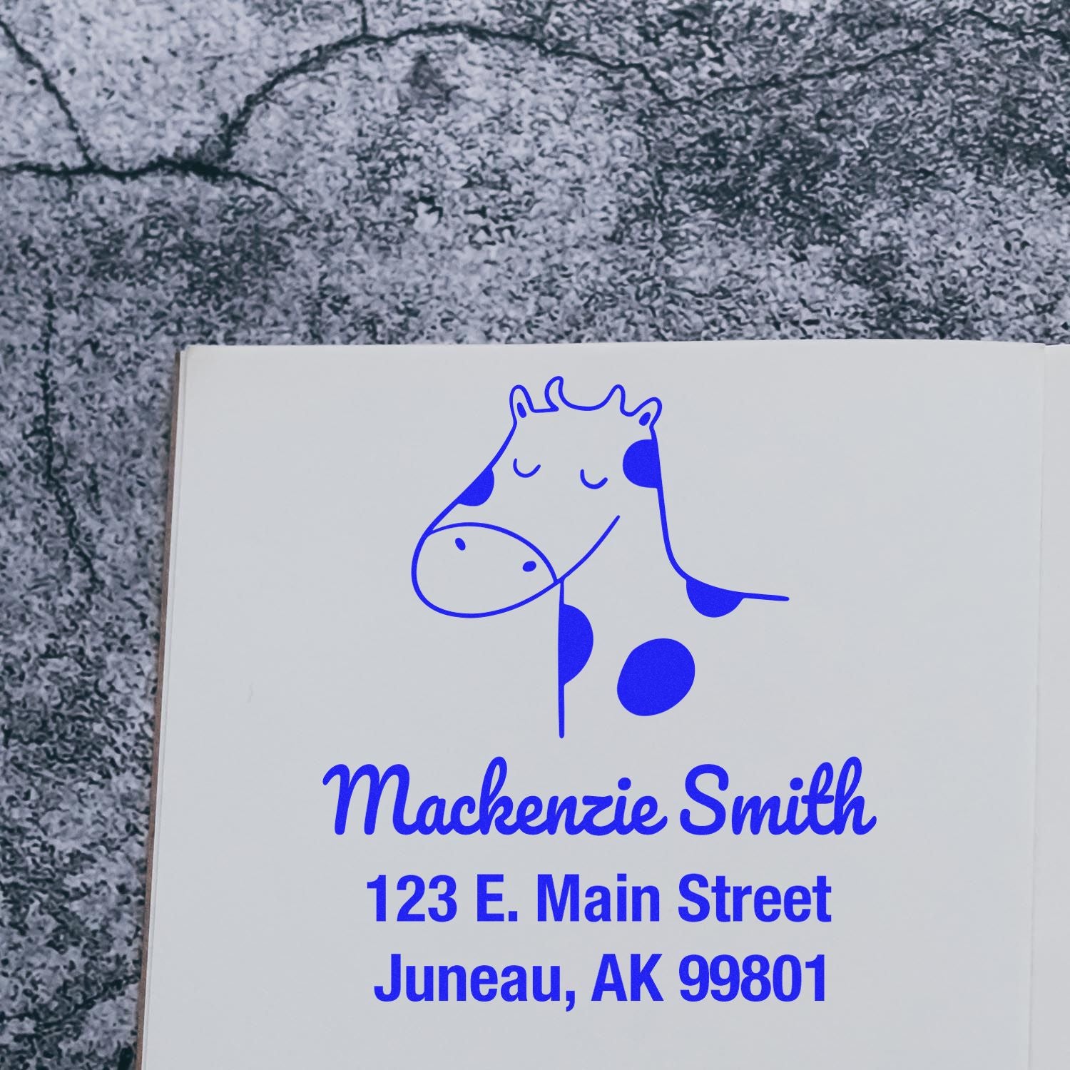 Wood handle stamp featuring a cartoon cow with the text "Mackenzie Smith, 123 E. Main Street, Juneau, AK 99801." This personalizable new address stamp is made to order, perfect for home use and cow cuddles enthusiasts.