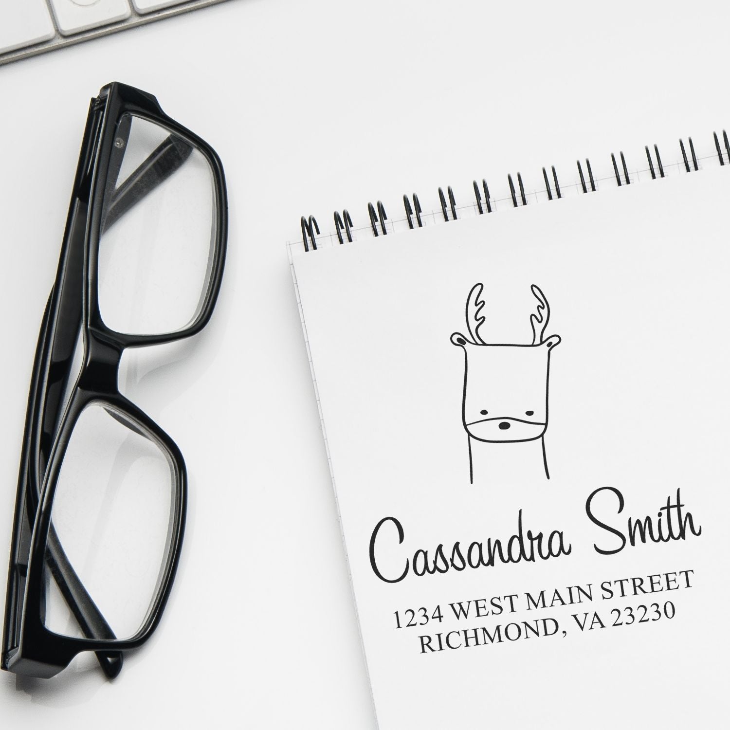 Self-Inking Cartoon Animal Regal Reindeer Custom Made Envelope Stamp displayed on a notepad with the name "Cassandra Smith" and address. Glasses and a keyboard are nearby. Customized Return Mail Stamp design is featured prominently.