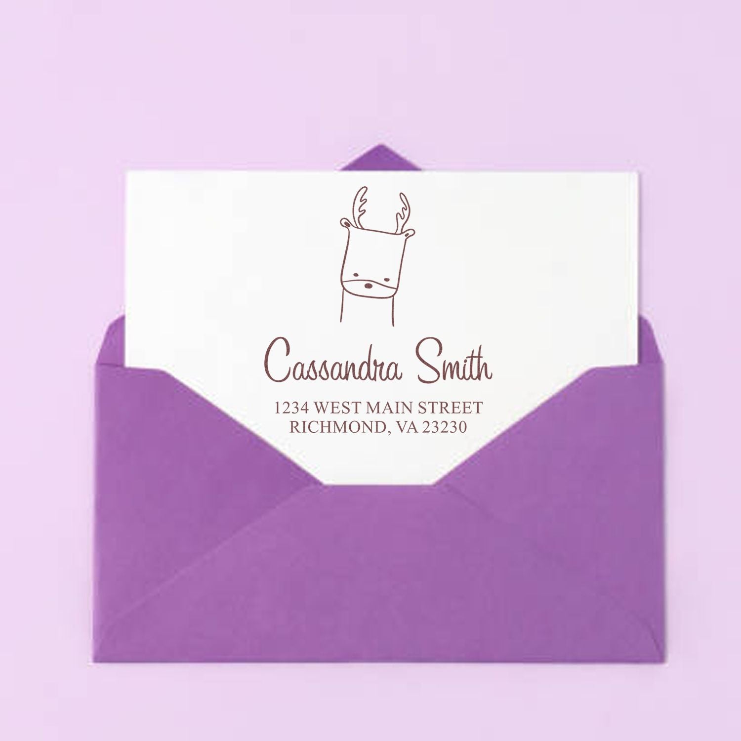 Purple envelope with a white card featuring a wood handle regal reindeer cartoon animal made to order envelope stamper. The personalized return mail stamp displays "Cassandra Smith, 1234 West Main Street, Richmond, VA 23230" in elegant font.