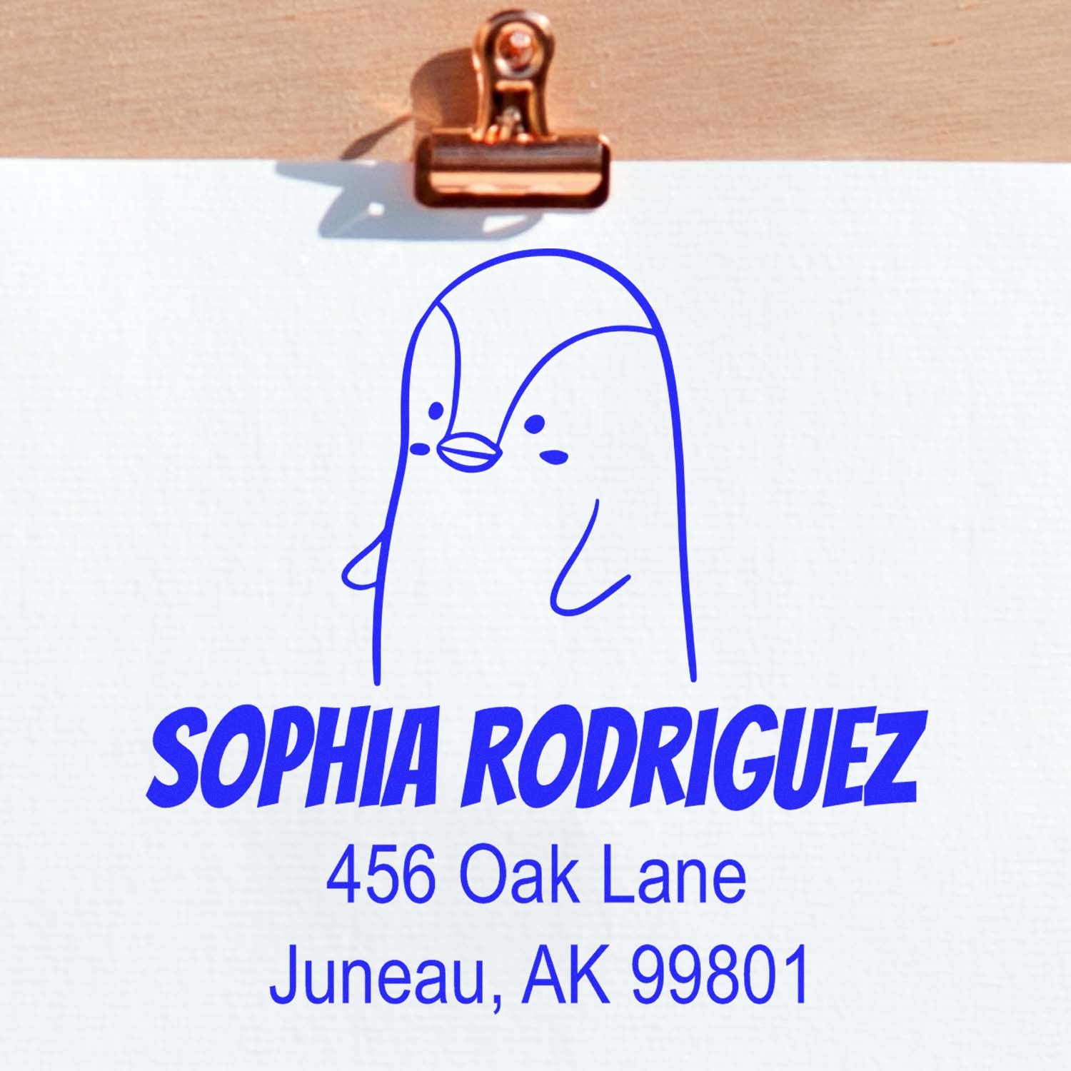 Wood handle perky penguin cartoon animal made to order address stamp on white paper. Custom return mail stamp features a blue penguin design with the name "Sophia Rodriguez" and address "456 Oak Lane, Juneau, AK 99801" in bold blue text.