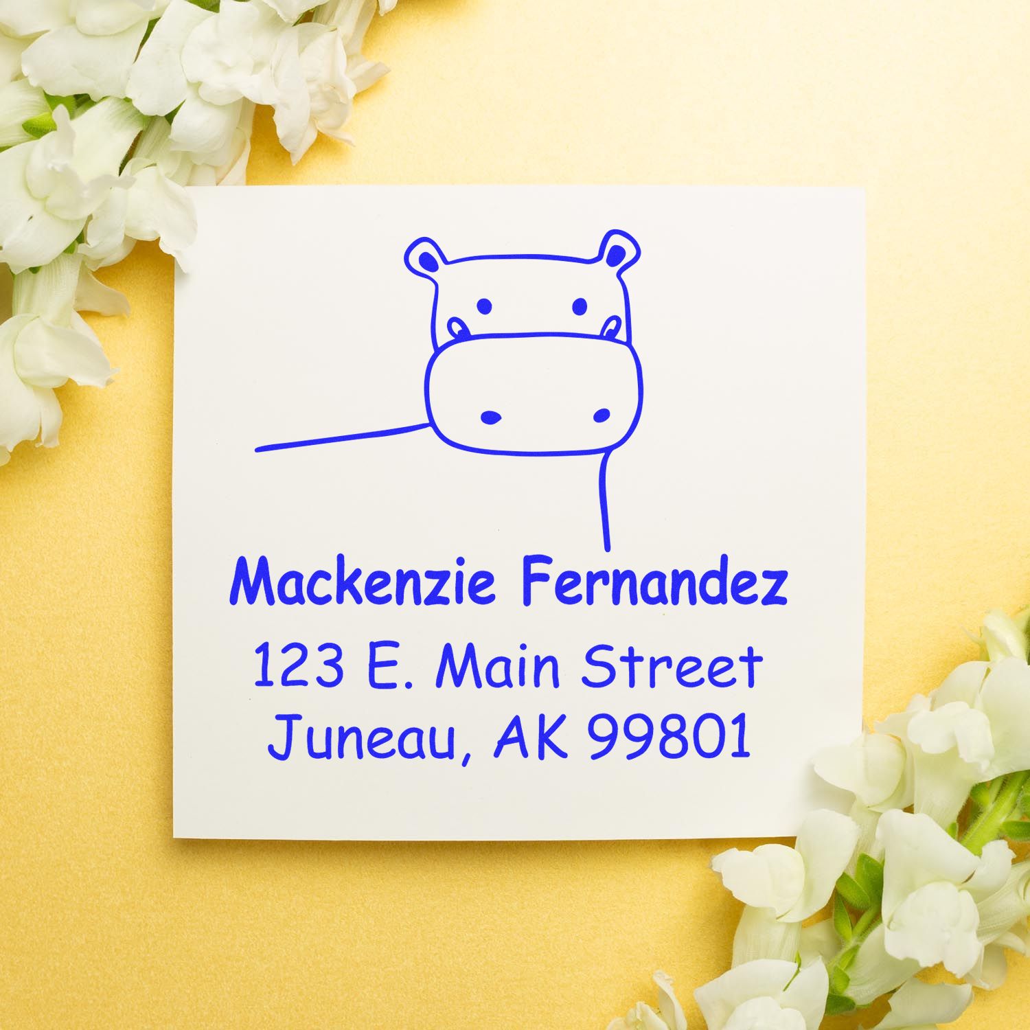 Portable Pre-Inked Happy Hippo Custom Designed Envelope Stamp on a white envelope with blue ink. The personalizable mailing stamp features a hippo illustration and address details, set against a gold background with white flowers.