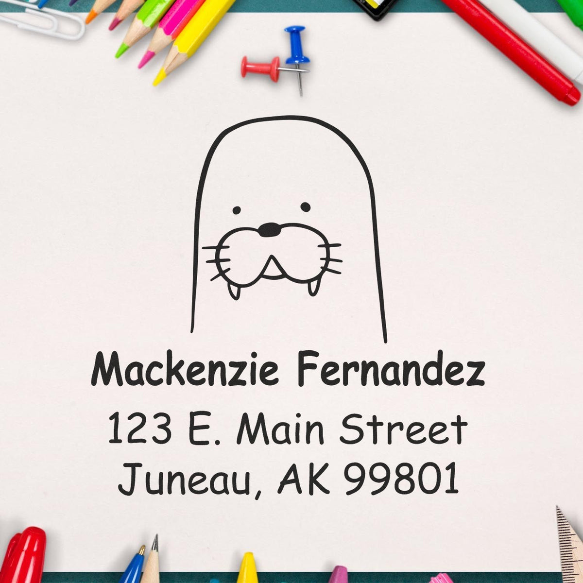 Wacky Walrus Pre-Inked Customized Return Address Stamp on paper with "Mackenzie Fernandez, 123 E. Main Street, Juneau, AK 99801" text. Surrounded by colorful stationery, showcasing the Custom Home Stamper design.