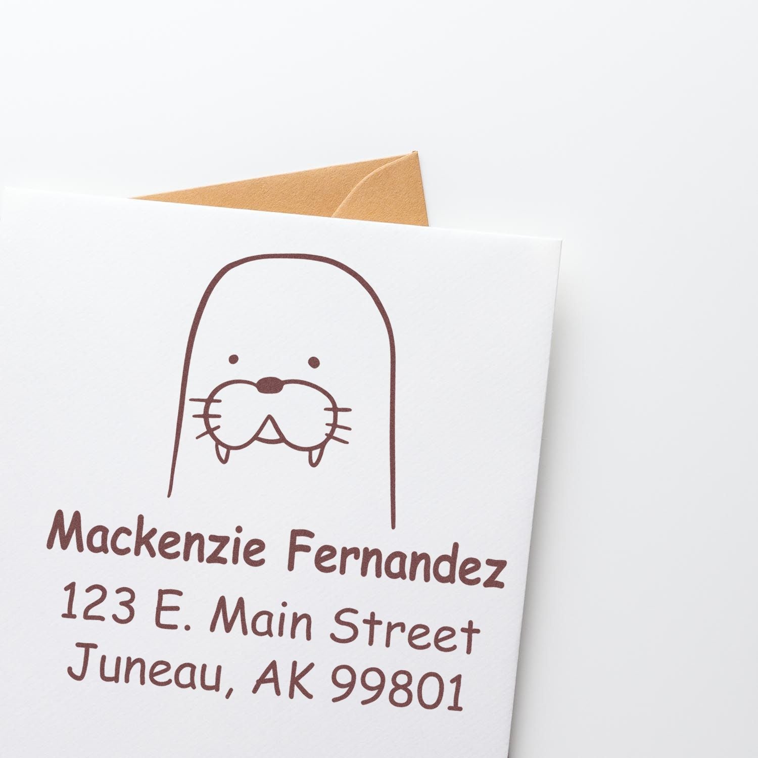 A Portable Pre-Inked Wacky Walrus Custom Designed Name And Address Stamper is shown in use on a white card. The stamp features a walrus illustration with customizable new address details, including a name and address in brown ink.