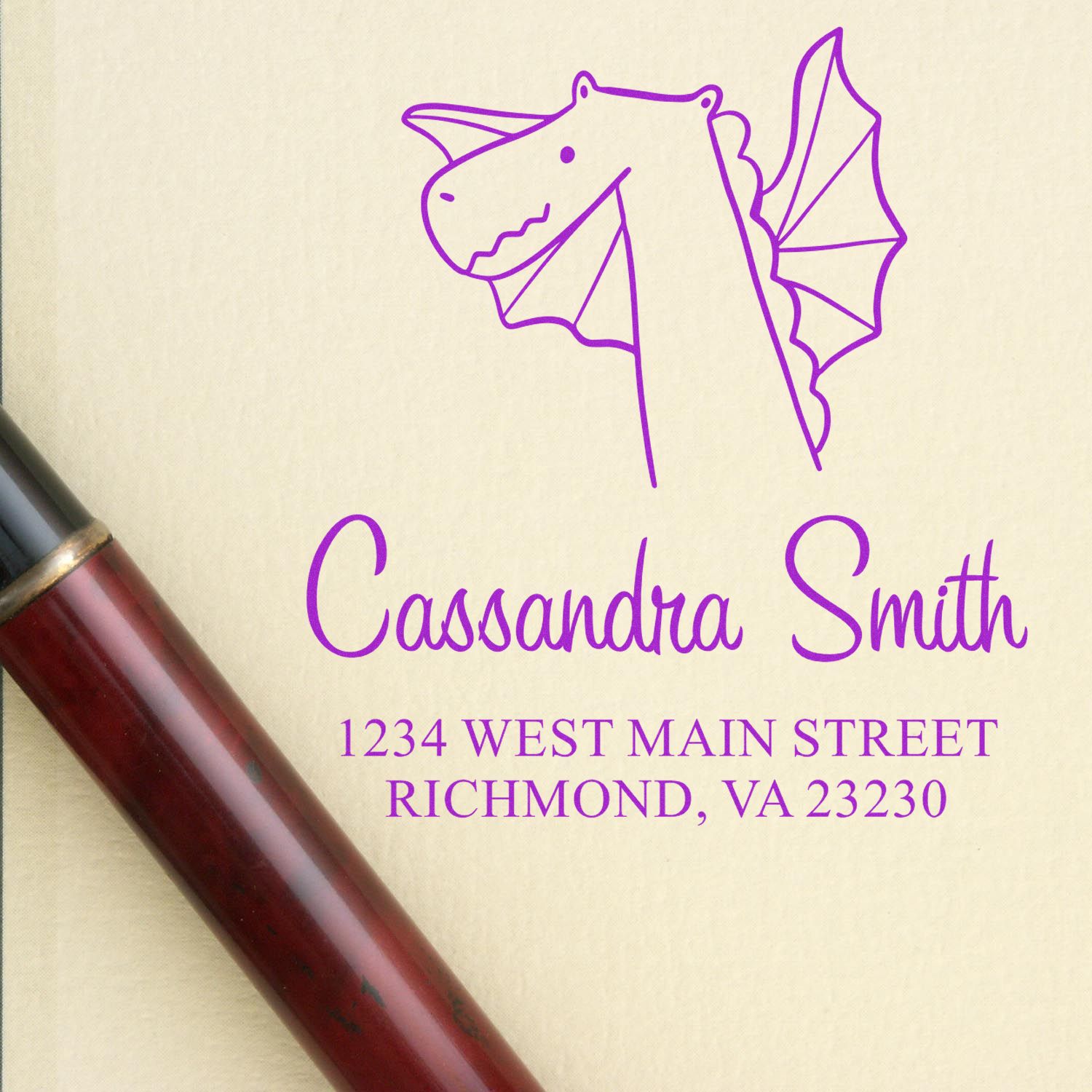 A Dragon Delight Pre-Inked Customized Home Address Stamper is shown on a beige background. The stamp features a purple dragon design above the name "Cassandra Smith" and address. This Custom-Made Address Stamp is next to a red and black pen.