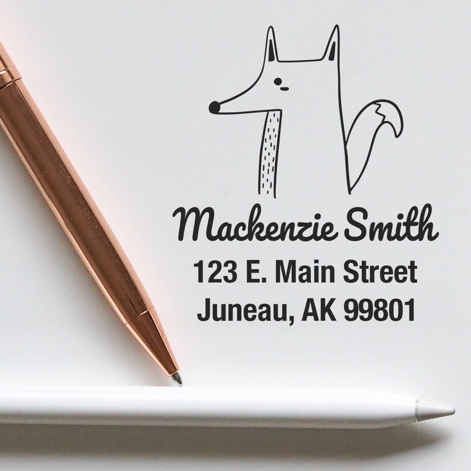 Self-Inking Cartoon Animal Finicky Fox Personalized Address Stamp featuring a fox illustration and the name Mackenzie Smith with address details. Customized New Address Stamp shown next to a rose gold pen and white pencil on a white surface.
