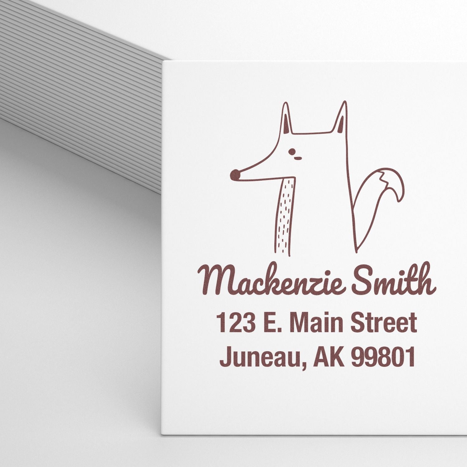 Wood handle finicky fox cartoon animal custom address stamper in use, displaying a customizable address stamp with the name Mackenzie Smith and address 123 E. Main Street, Juneau, AK 99801 on white paper.