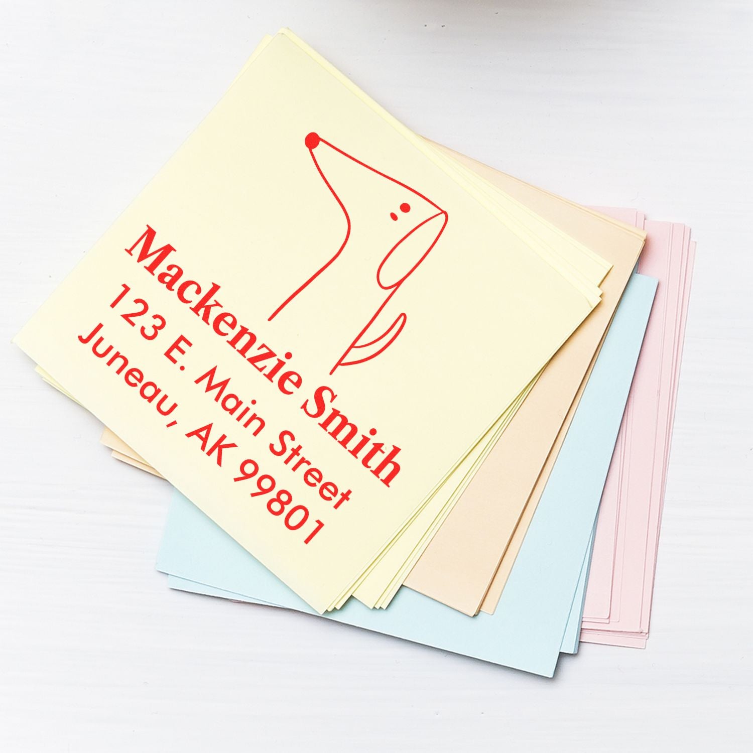 Wood handle custom-made mailing stamp featuring a perky pooch cartoon animal design. The stamp is shown in use on a stack of pastel-colored envelopes, with red ink displaying an address and the dog illustration.