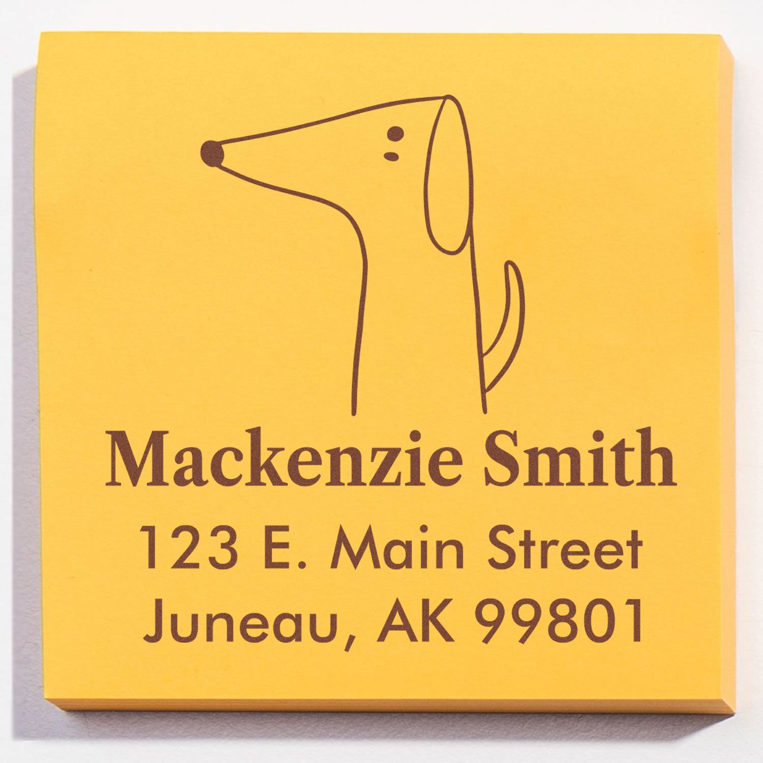 Yellow notepad with a Self-Inking Cartoon Animal Perky Pooch Personalized Address Stamper design. Features a simple dog illustration above the text "Mackenzie Smith, 123 E. Main Street, Juneau, AK 99801." Ideal for a Custom Address Stamp.