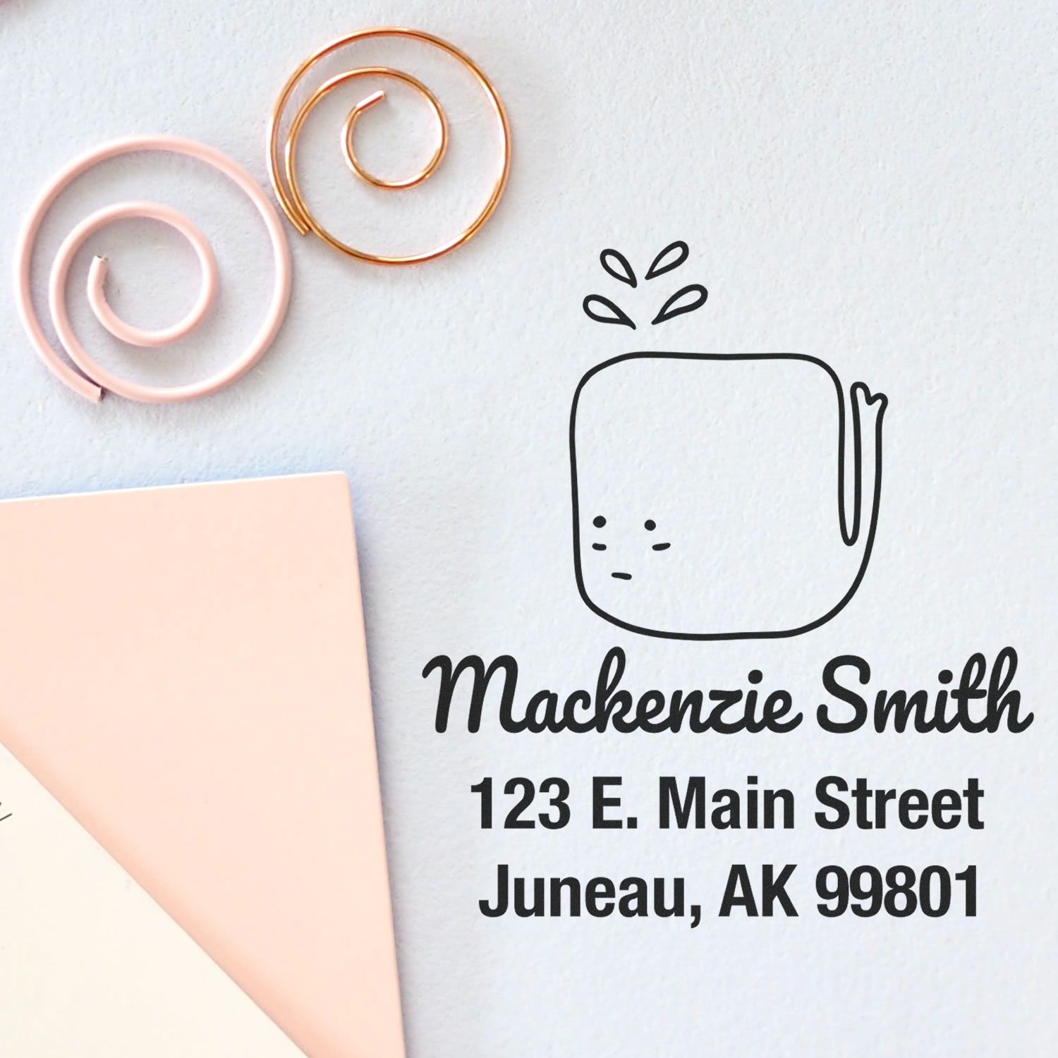 Portable Pre-Inked Joyful Whale Made To Order Mailing Stamper featuring a cute whale design with personalized return mail stamper details: "Mackenzie Smith, 123 E. Main Street, Juneau, AK 99801" on a light background with decorative spirals.
