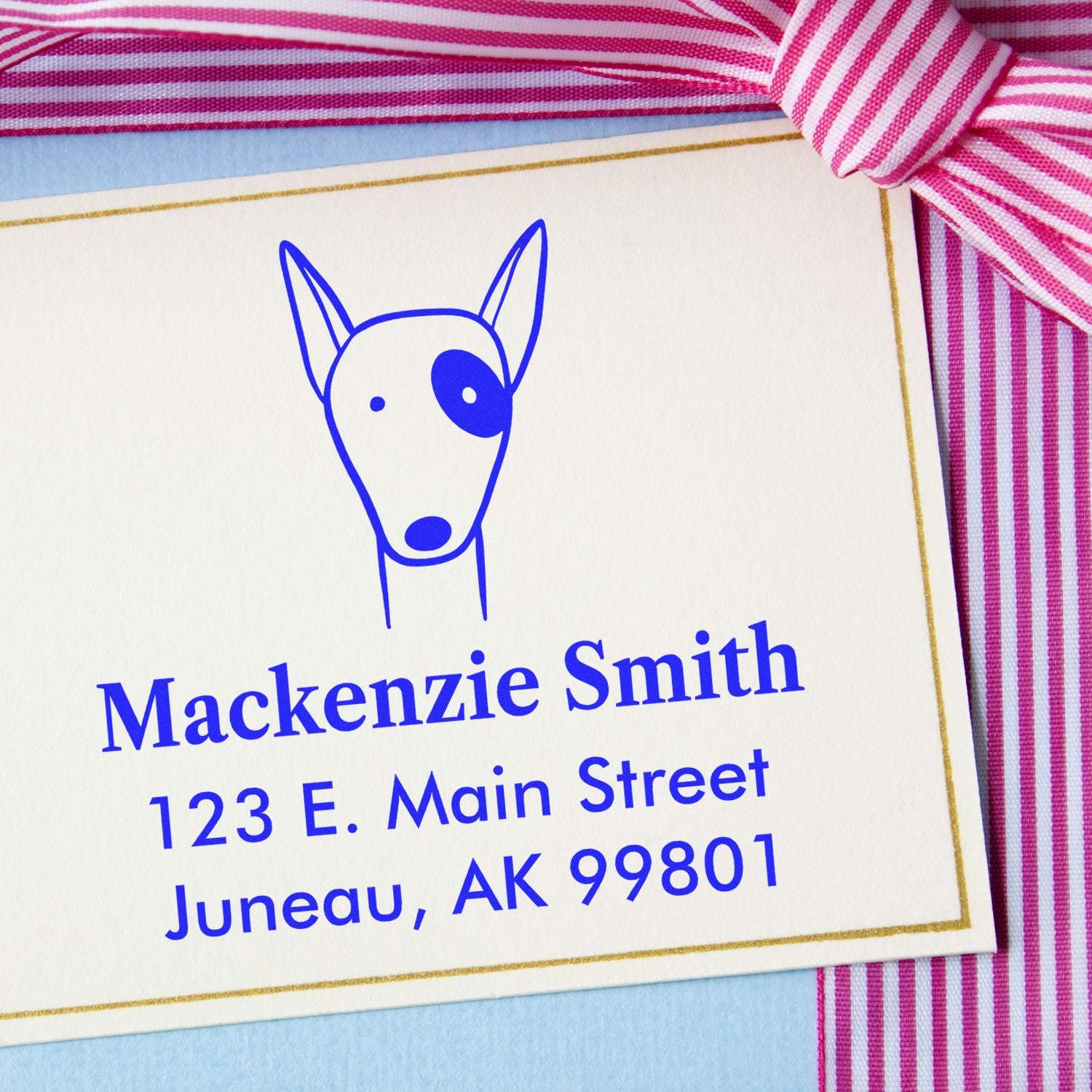 Portable Pre-Inked Delightful Dog Made To Order Address Stamp on a card with a dog illustration, personalized with the name Mackenzie Smith and address 123 E. Main Street, Juneau, AK 99801. Personalized Mailing Stamp with pink striped ribbon.