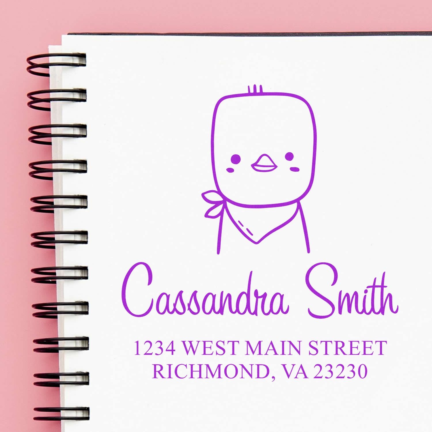 A spiral notebook on a pink background features a Cute Chick Pre-Inked Handcrafted Home Stamp design. The Customized Return Mail Stamper displays the name "Cassandra Smith" and an address in Richmond, VA, in purple ink.