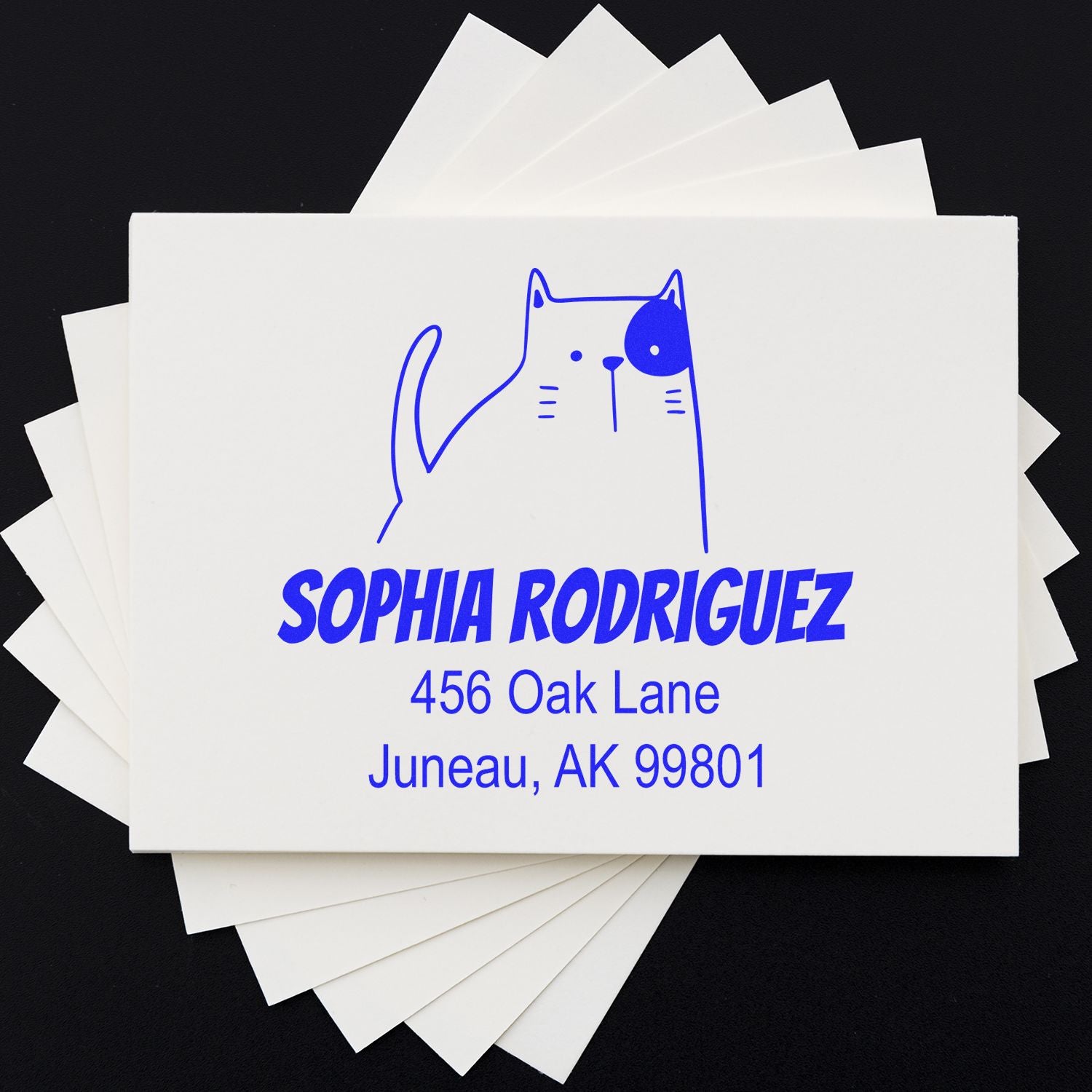 A stack of cards featuring a blue Fluffy Feline Pre-Inked Handcrafted Home Stamper design with a cat illustration. The Personalizable Mailing Stamper displays the name "Sophia Rodriguez" and an address in Juneau, AK.