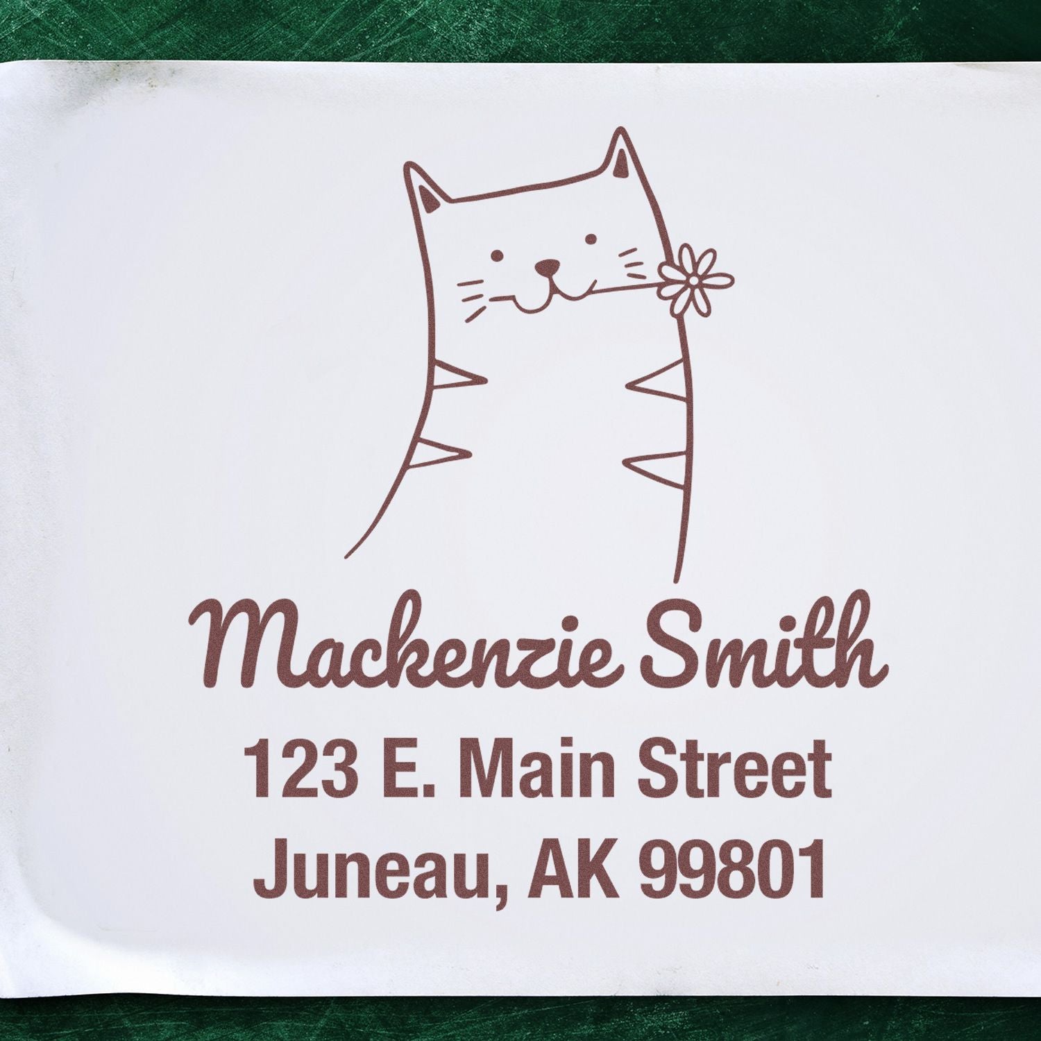 Portable Pre-Inked Happy Cat Made To Order Envelope Stamp featuring a cute cat with a flower, above the name Mackenzie Smith and address 123 E. Main Street, Juneau, AK 99801. This Custom Address Stamper is displayed on a white envelope.