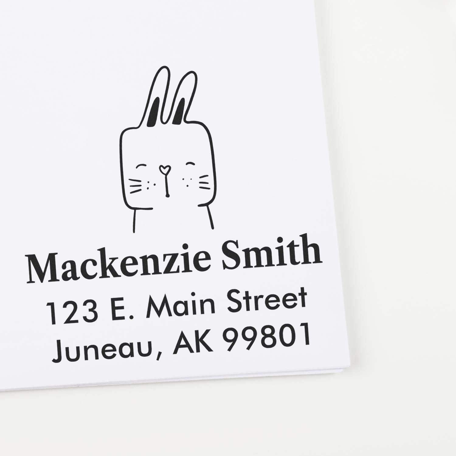 Self-Inking Cartoon Animal Fuzzy Rabbit Personalized Address Stamper on white paper, featuring a cute rabbit illustration above the custom-made new address stamp with the name "Mackenzie Smith" and address "123 E. Main Street, Juneau, AK 99801".
