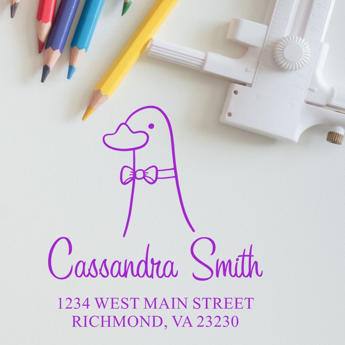 Wood Handle Dashing Duck Cartoon Animal Custom Name And Address Stamper on paper with "Cassandra Smith, 1234 West Main Street, Richmond, VA 23230" in purple. Customizable New Address Stamp with colored pencils and a ruler nearby.