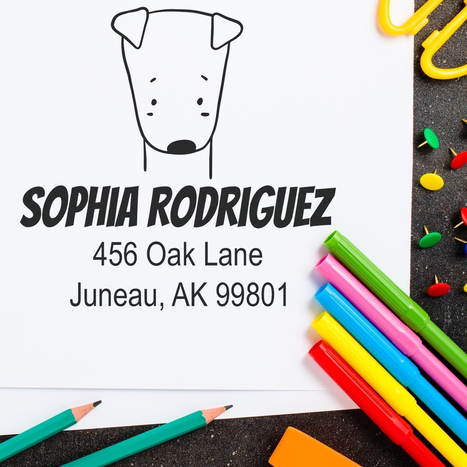 Wood Handle Daring Dog Cartoon Animal Custom Return Address Stamp on white paper with "Sophia Rodriguez, 456 Oak Lane, Juneau, AK 99801" text. Colorful pens and paperclips surround the Customized Return Mail Stamp.