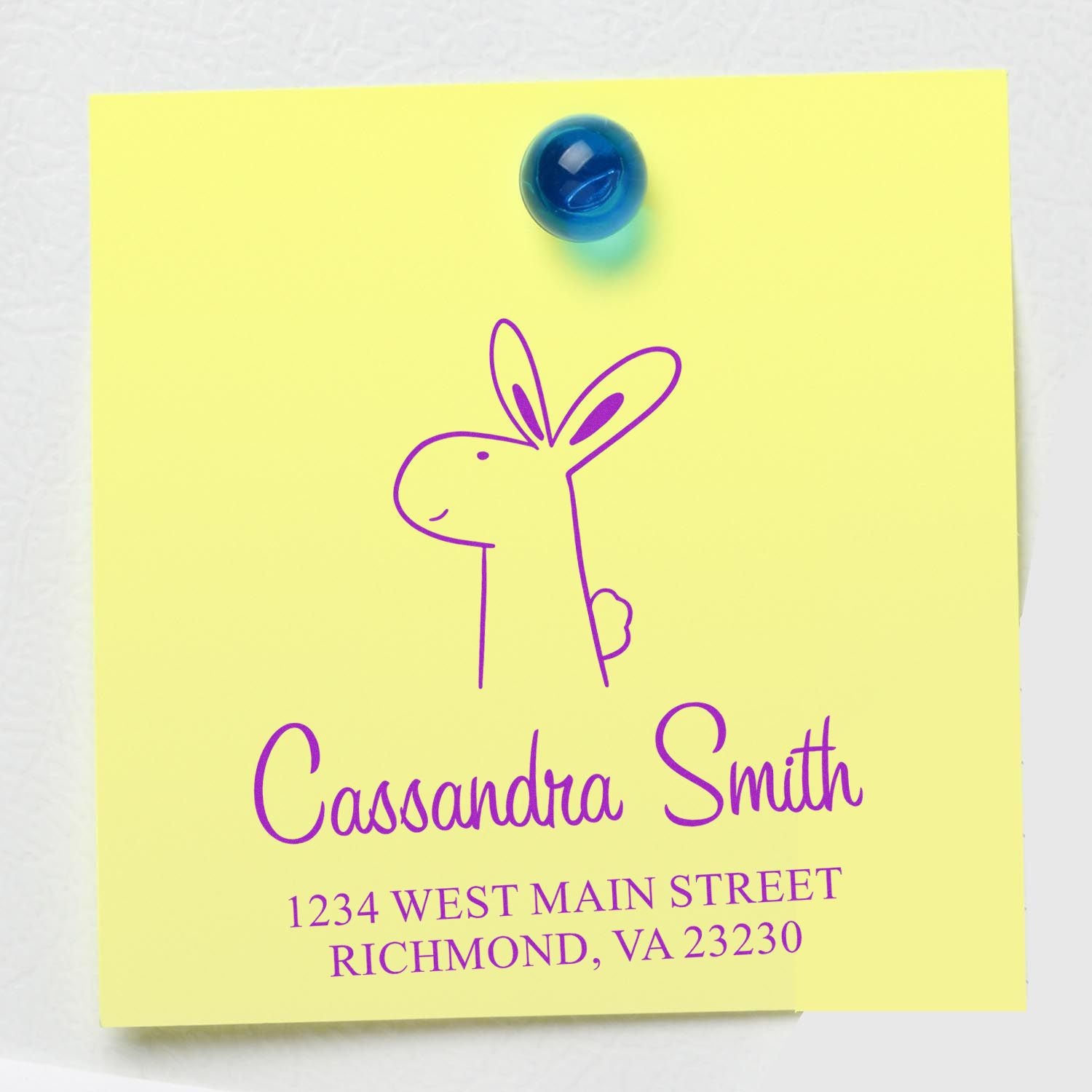 Yellow note with a purple Bouncy Bunny Pre-Inked Handcrafted Home Address Stamp design, featuring a bunny illustration. Text reads "Cassandra Smith, 1234 West Main Street, Richmond, VA 23230." Personalizable Home Stamp pinned with a blue magnet.